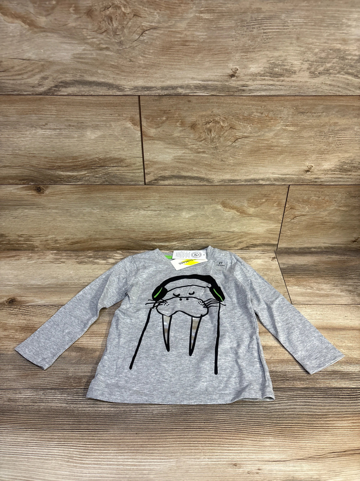 Flat lay of Epic Threads grey long-sleeve toddler shirt size 2T showing walrus wearing headphones graphic on wood background
