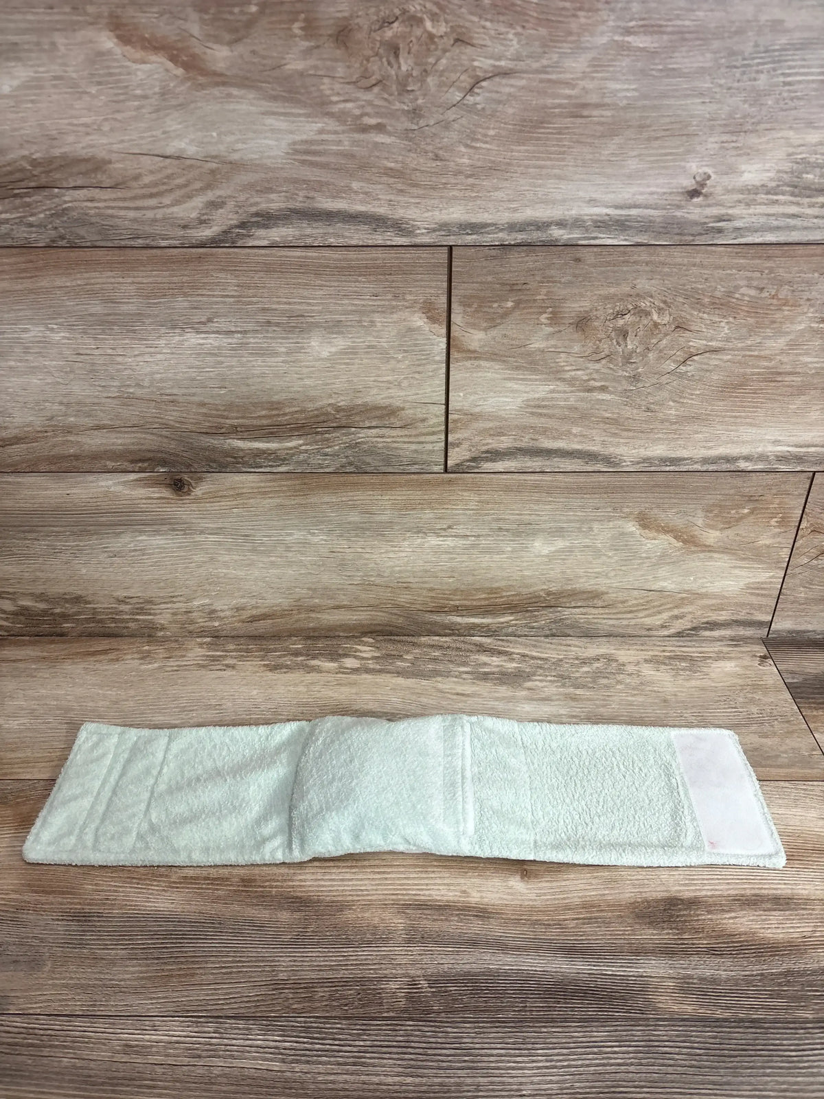Top view of Dr. Brown’s Infant Gripebelt heated belly band in light green terry with Velcro closure on wood background