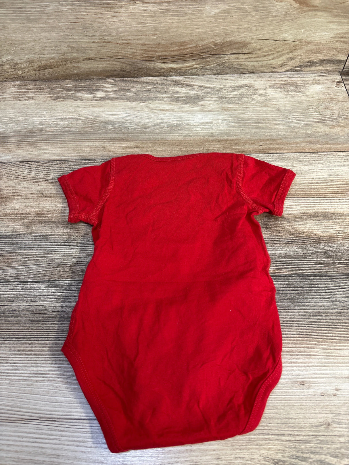 Back view of Bluey Snickers red short-sleeve baby bodysuit (6-12 months) laid flat on wood surface showing plain back and stitching