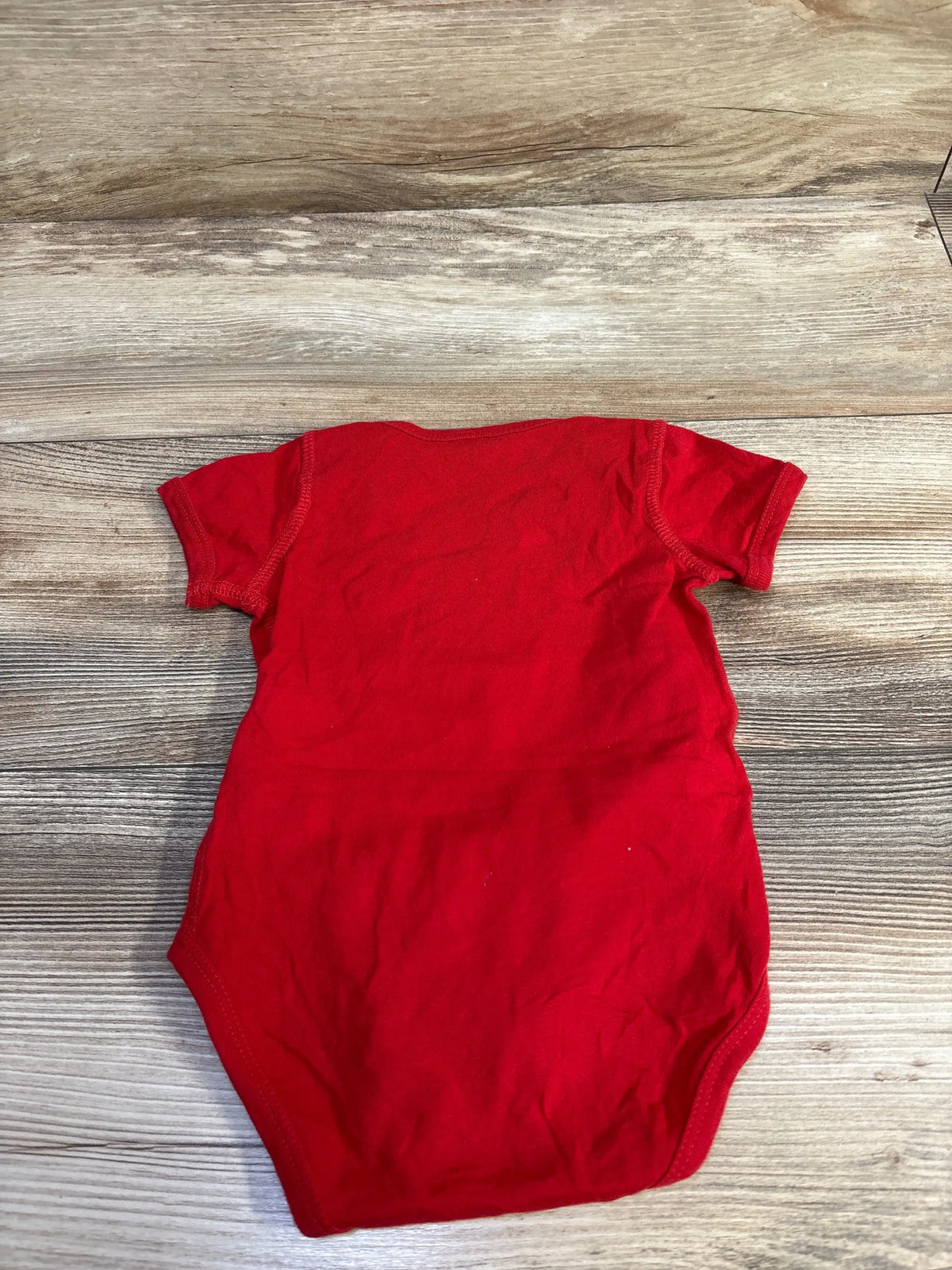 Back view of Bluey Snickers red short-sleeve baby bodysuit (6-12 months) laid flat on wood surface showing plain back and stitching