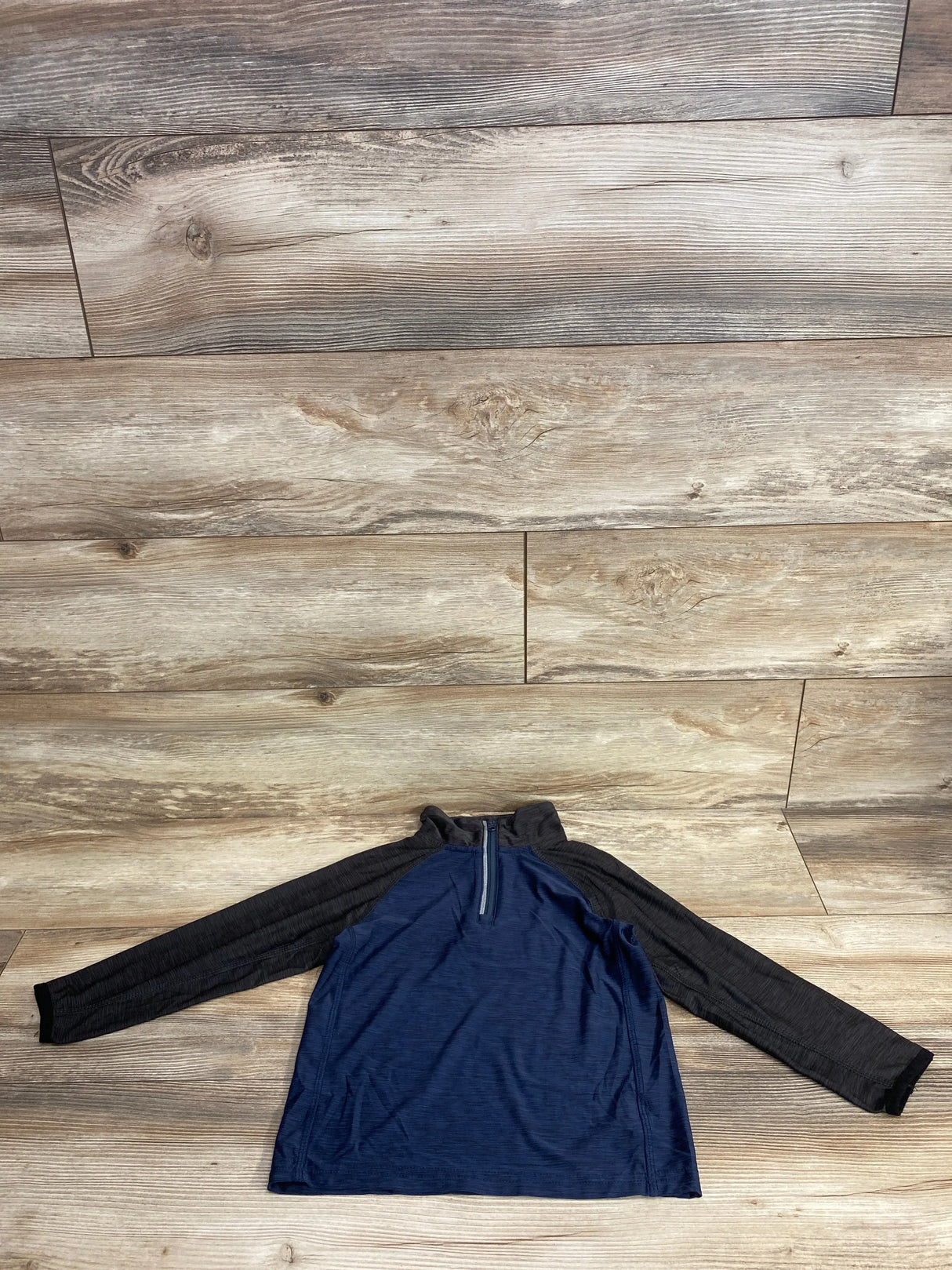 Children's long sleeve navy and black quarter zip shirt on wooden floor background