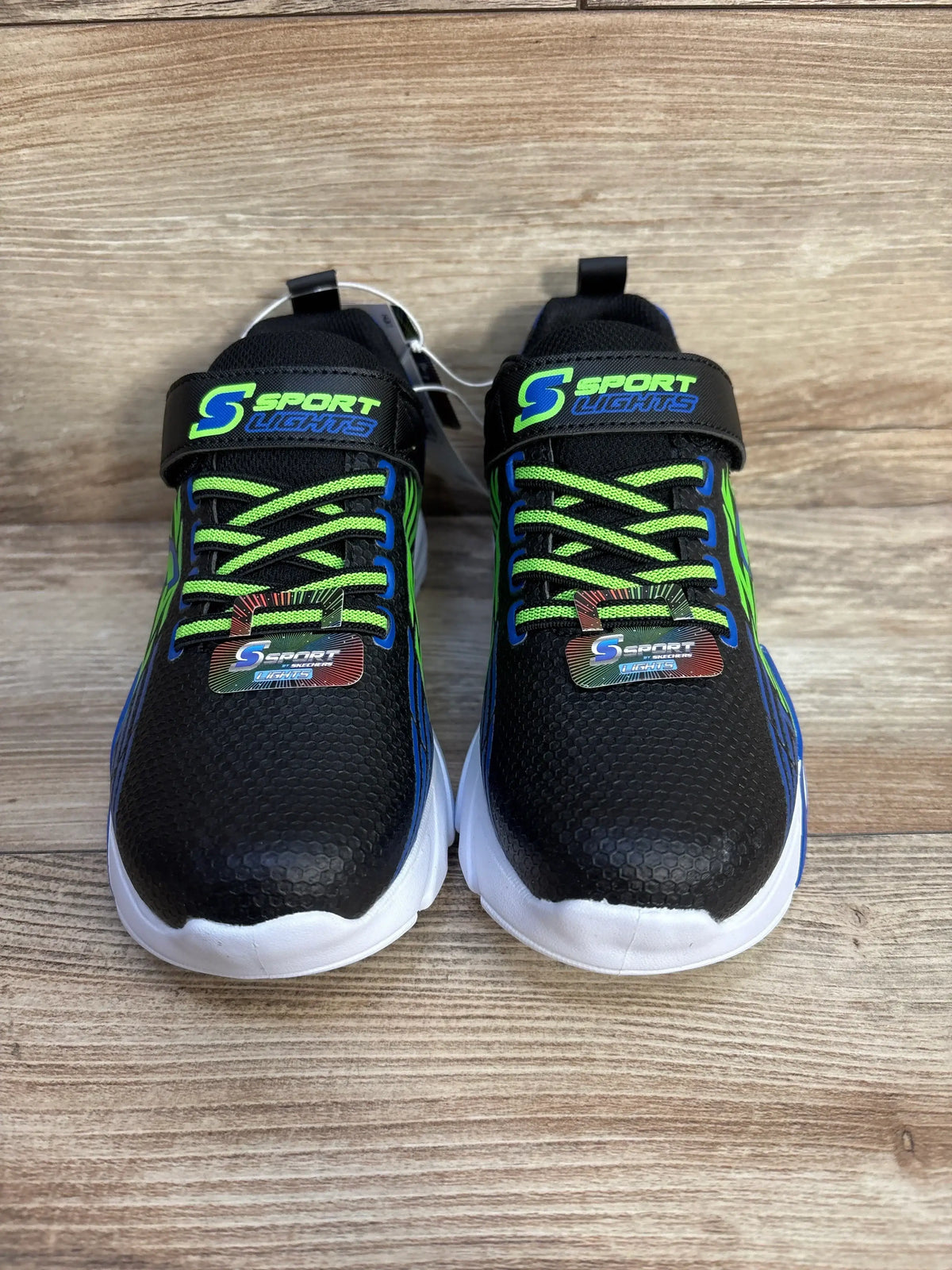 Top view of S Sport by Skechers Lights Ottis performance sneakers in black with neon green and blue accents and strap on wood plank background