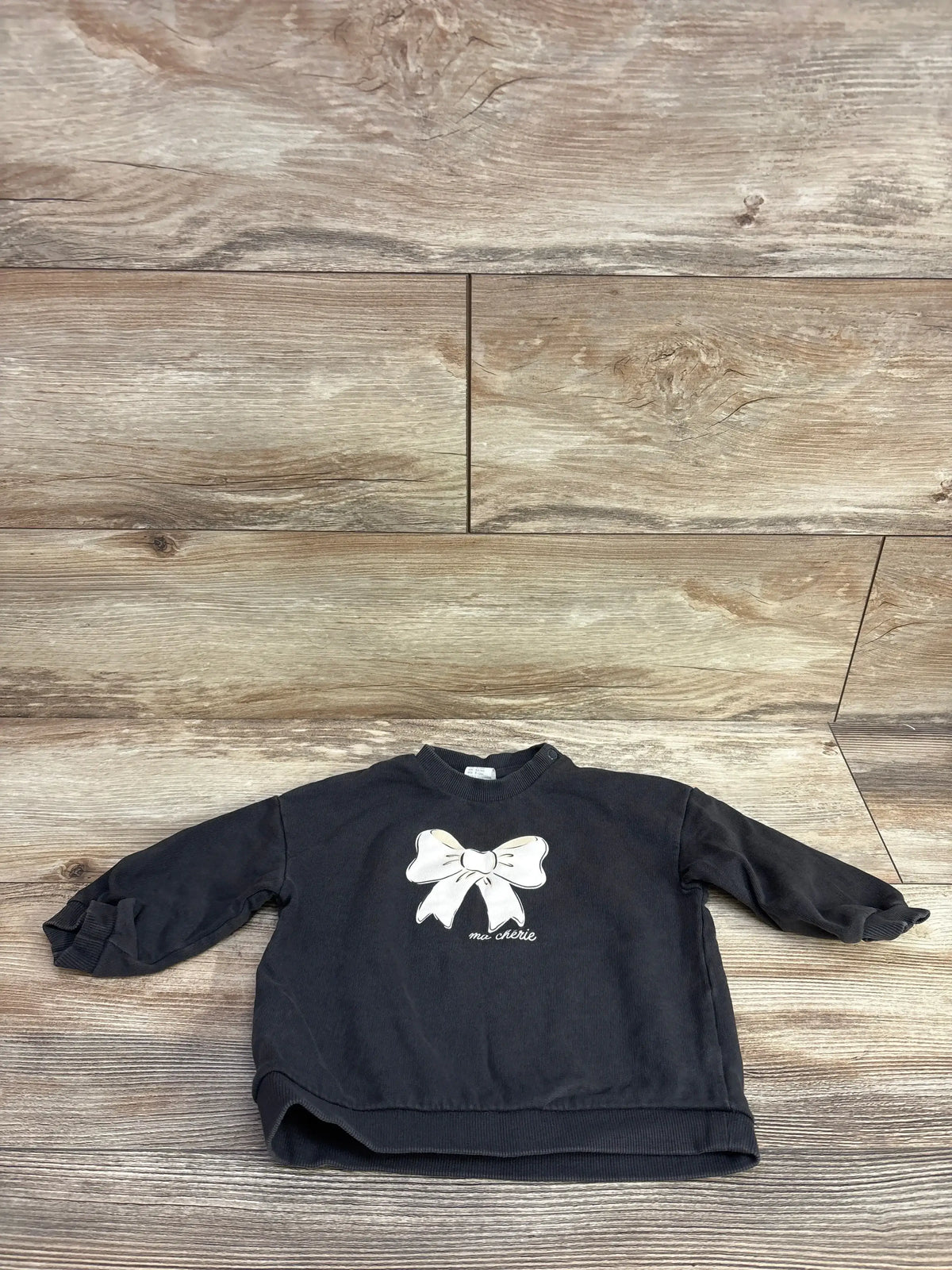 Black toddler sweatshirt with white bow and 'ma chérie' text on wooden floor
