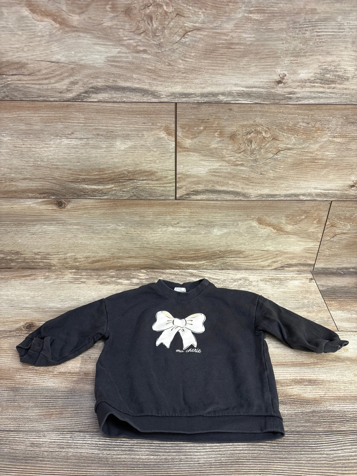 Black toddler sweatshirt with white bow and 'ma chérie' text on wooden floor