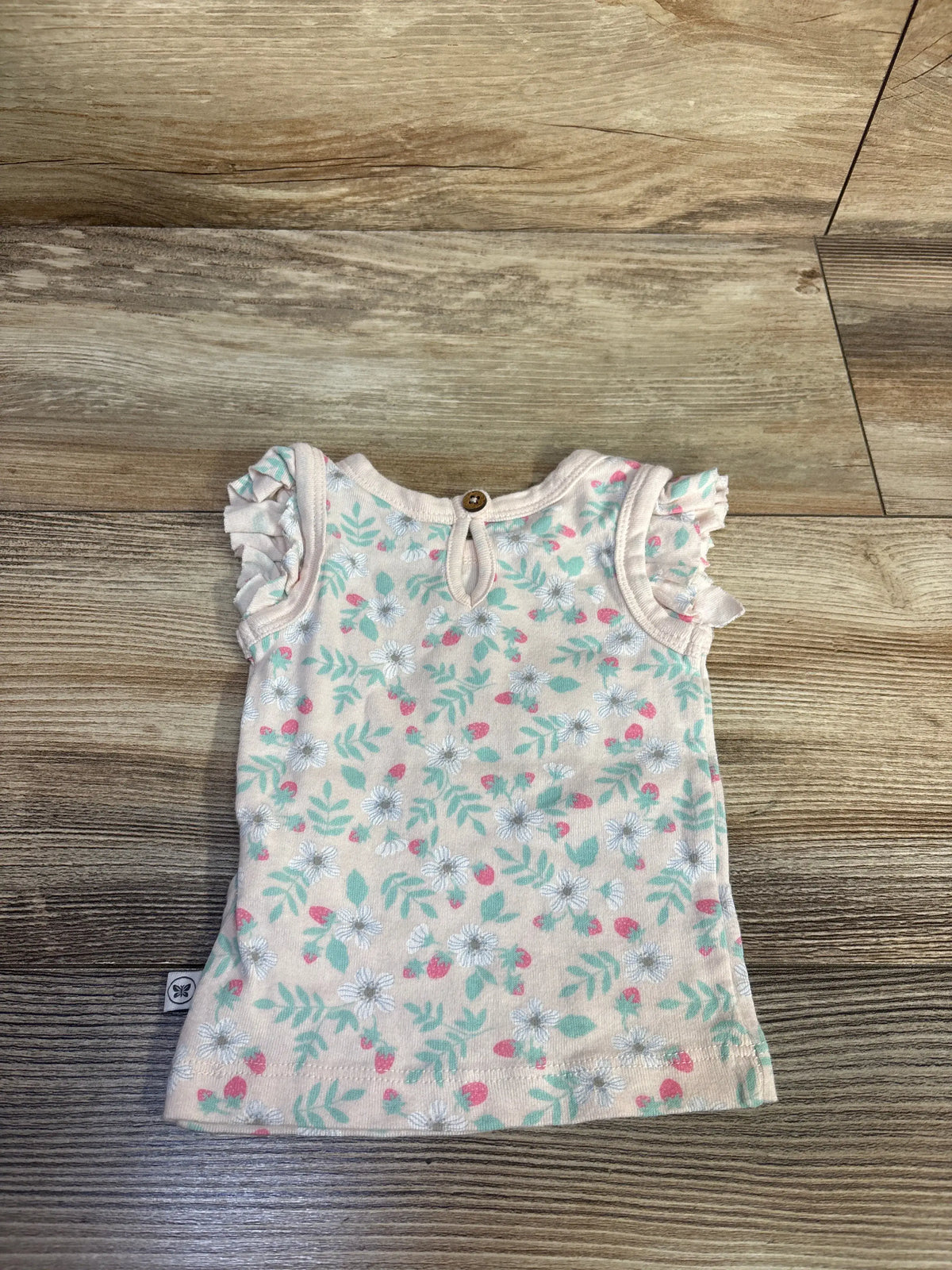 Front view of Honest Baby floral tank top in pink showcasing ruffled cap sleeves and button neckline on a wood-grain background