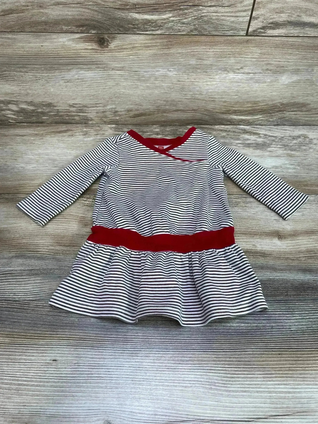 Flat lay of toddler striped twirl dress with red waistband and neckline, long sleeves on light wood background
