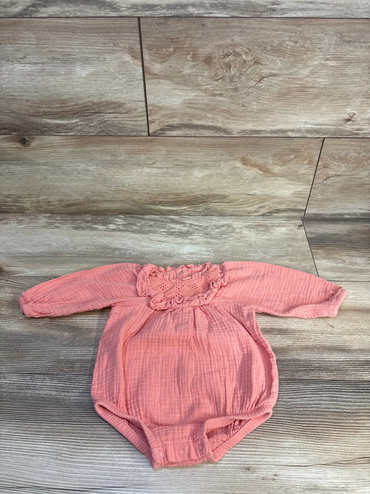 Pink baby onesie with long sleeves and ruffled neckline on wood floor