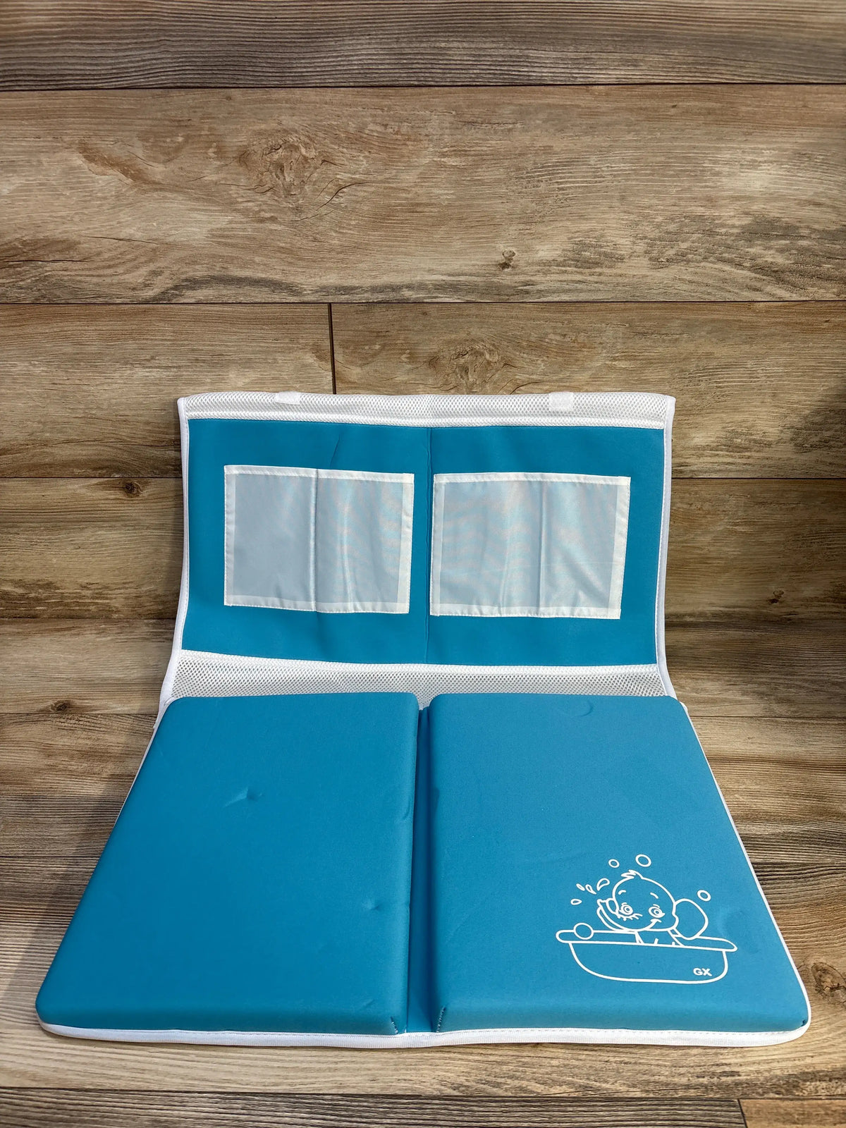 Open view of Gamexcel baby bath kneeler and elbow rest showcasing blue padding and mesh storage pockets on a wood floor