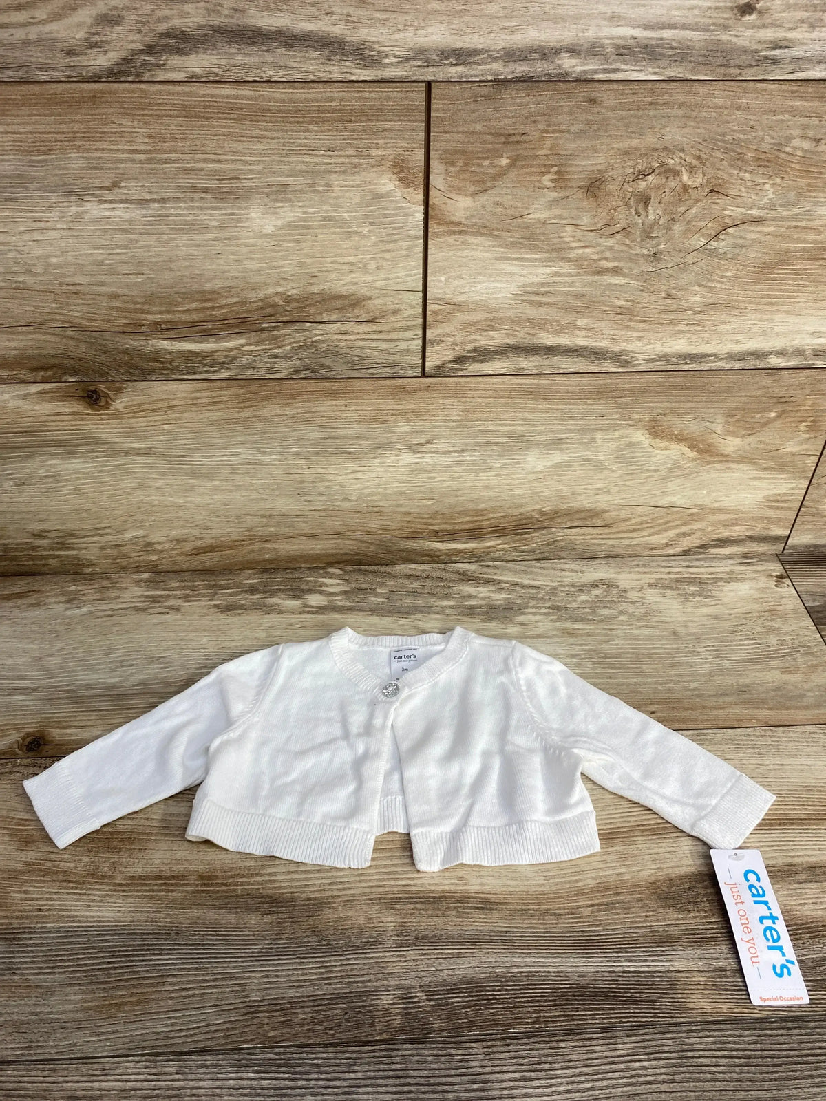 White long-sleeve baby cardigan from Carter's with single button and tag on wood background