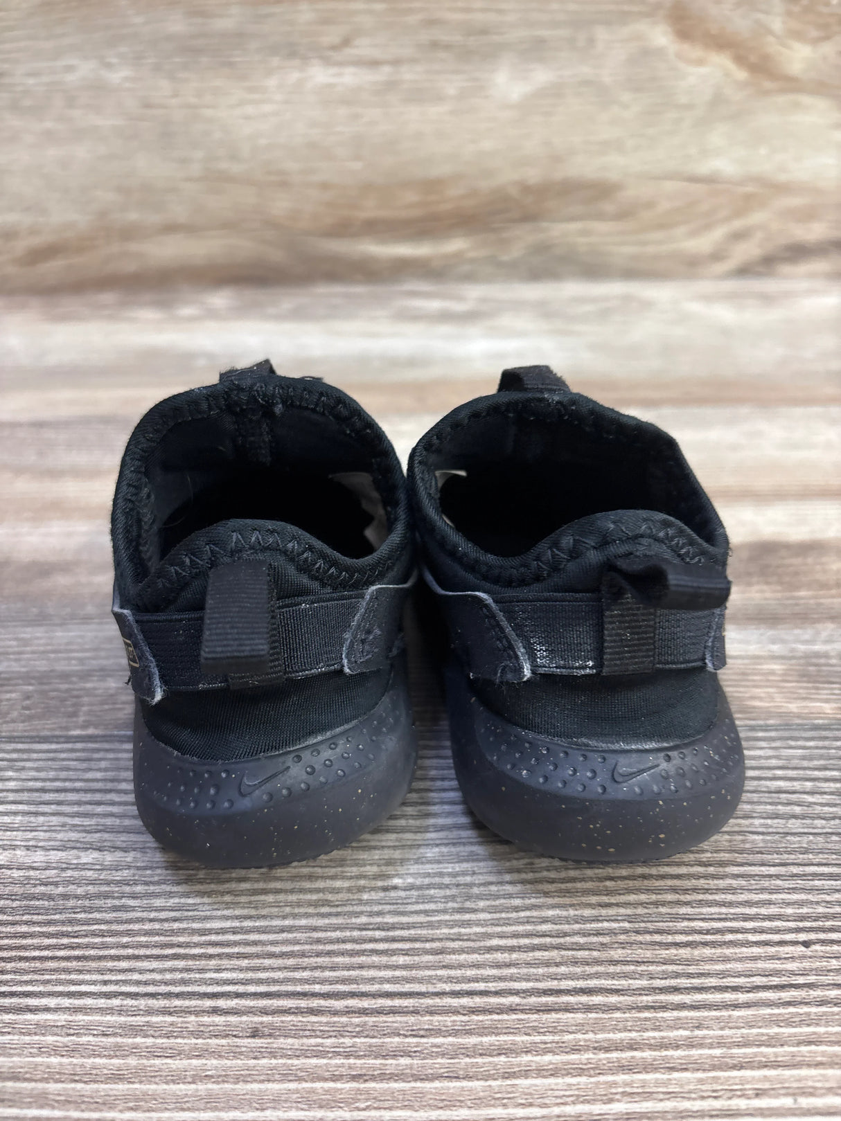 Rear view of Nike Flex Runner toddler sneakers showcasing heel pull tabs and speckled rubber outsoles on wood-grain background