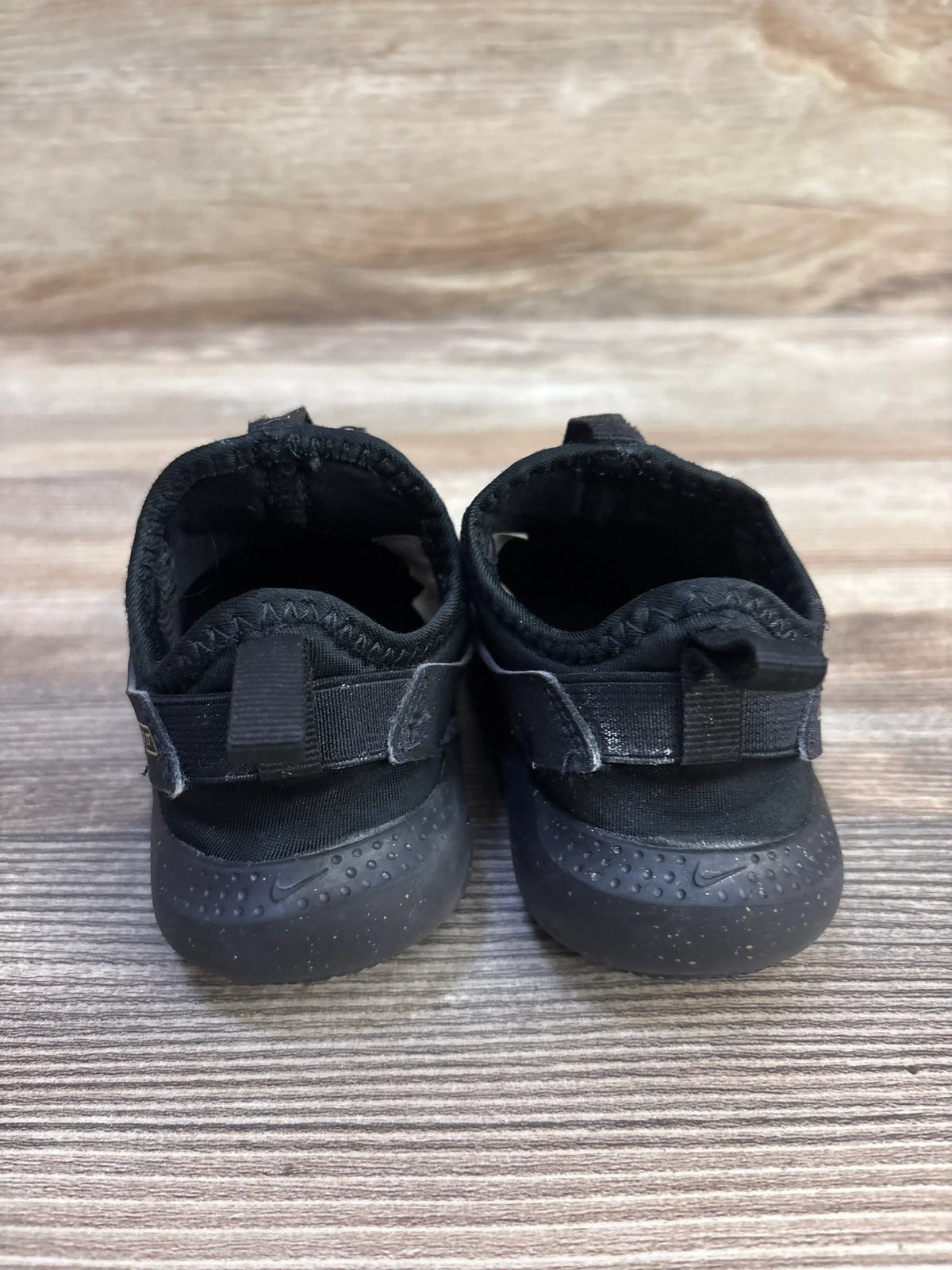 Rear view of Nike Flex Runner toddler sneakers showcasing heel pull tabs and speckled rubber outsoles on wood-grain background