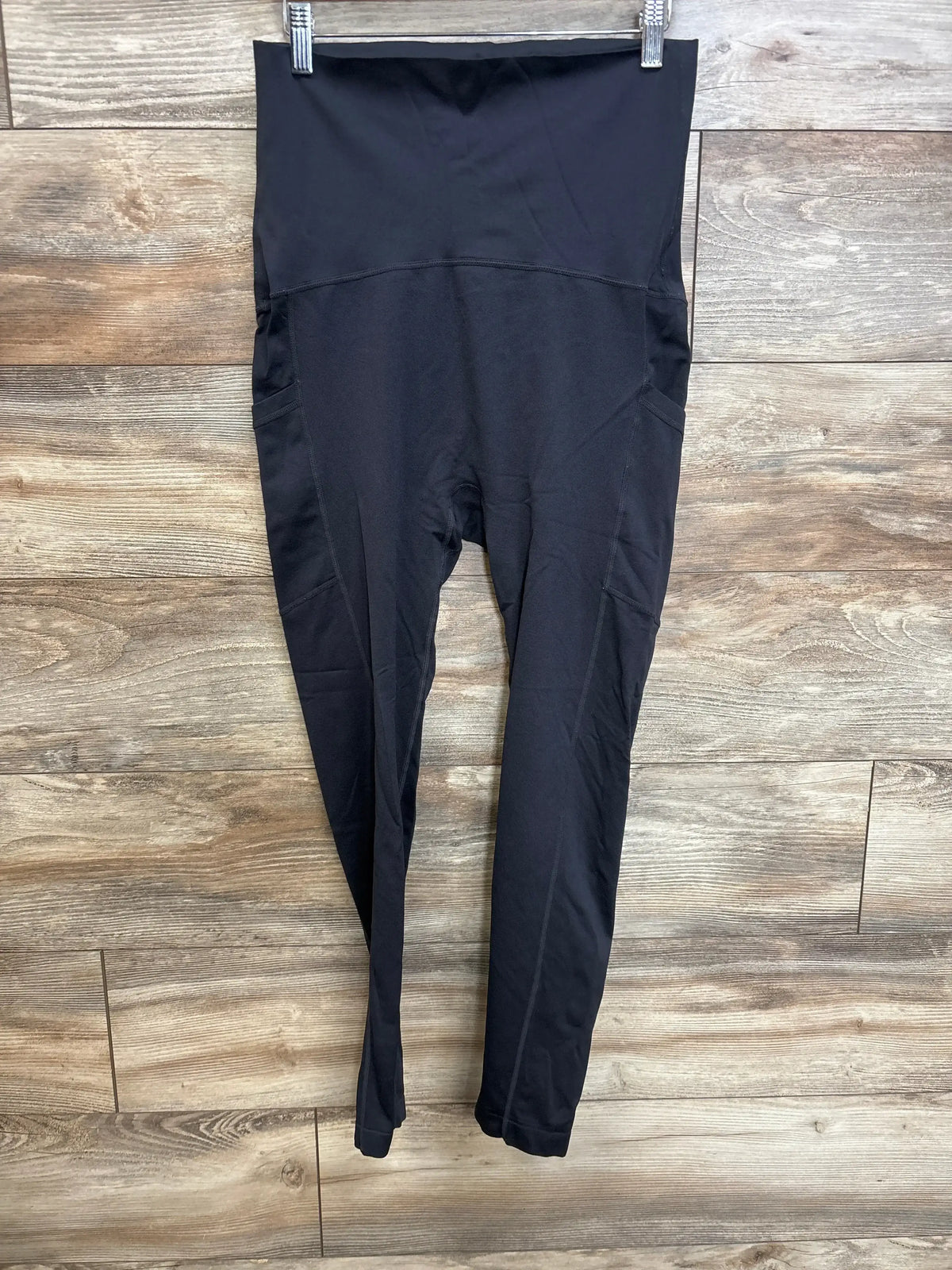 Front view of black maternity full panel leggings showing high-rise tummy panel and side pockets hanging against wooden background