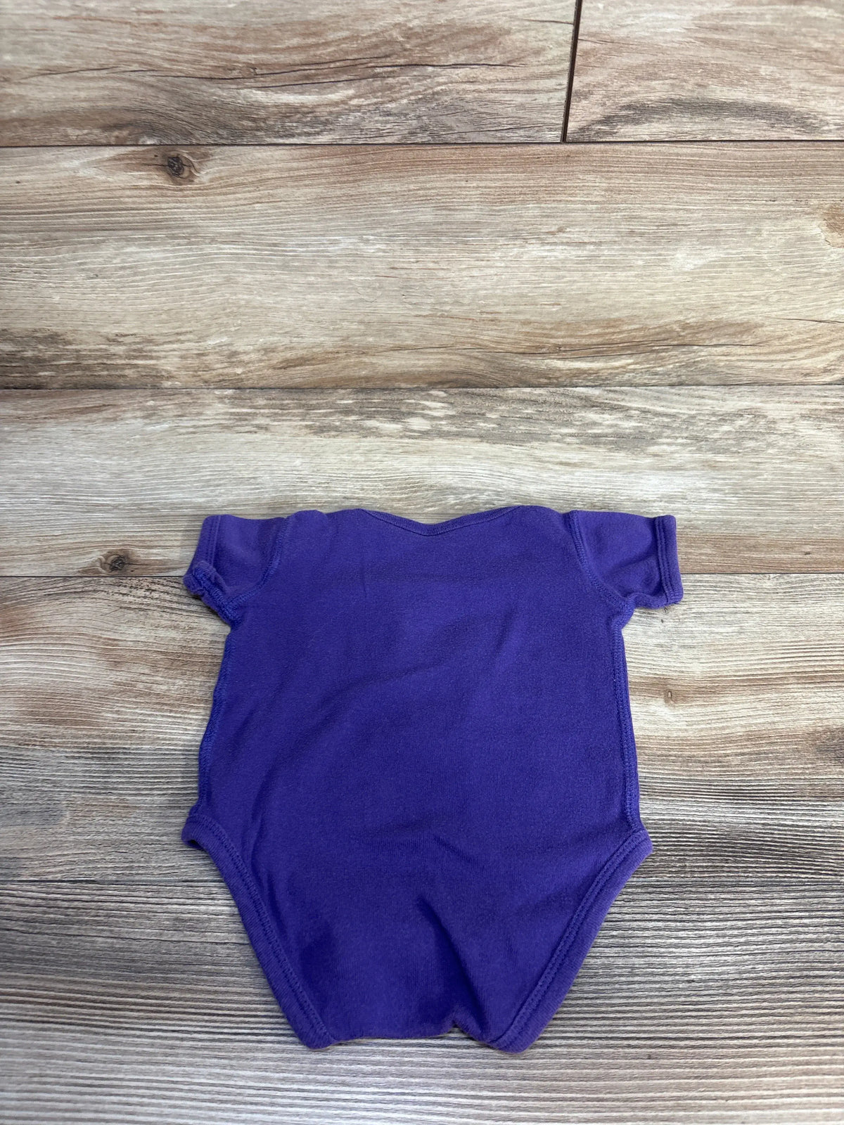 Back view of Outerstuff Minnesota Vikings bodysuit in purple, with short sleeves on a wood-grain background