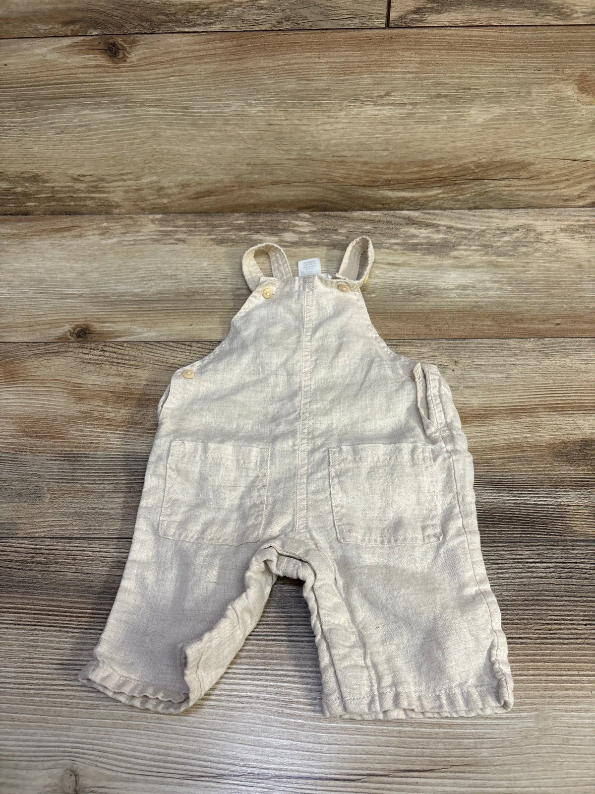 H&M newborn linen overalls in tan laid flat on a light wood background