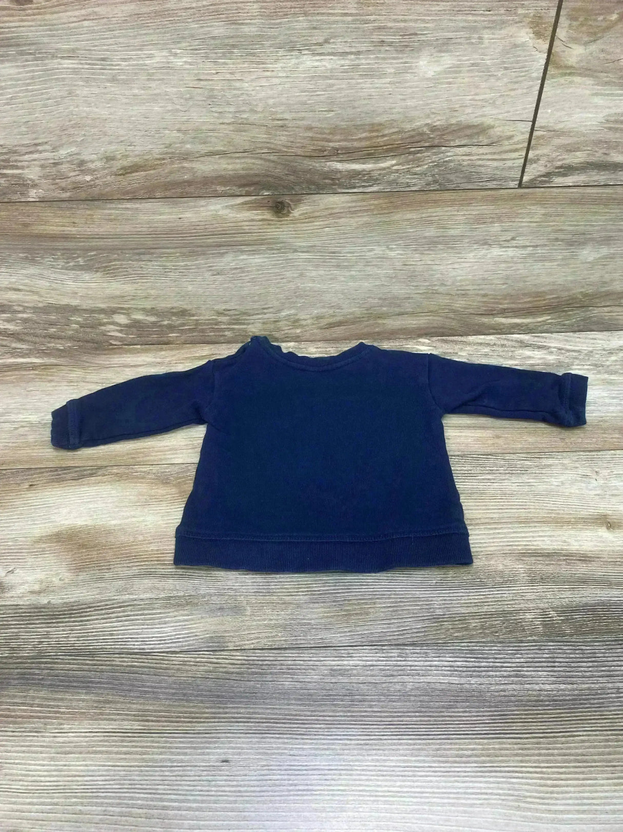 Flat lay of H&M navy baby sweatshirt showing long sleeves, ribbed hem, and crew neckline, size 4-6 months on wood background