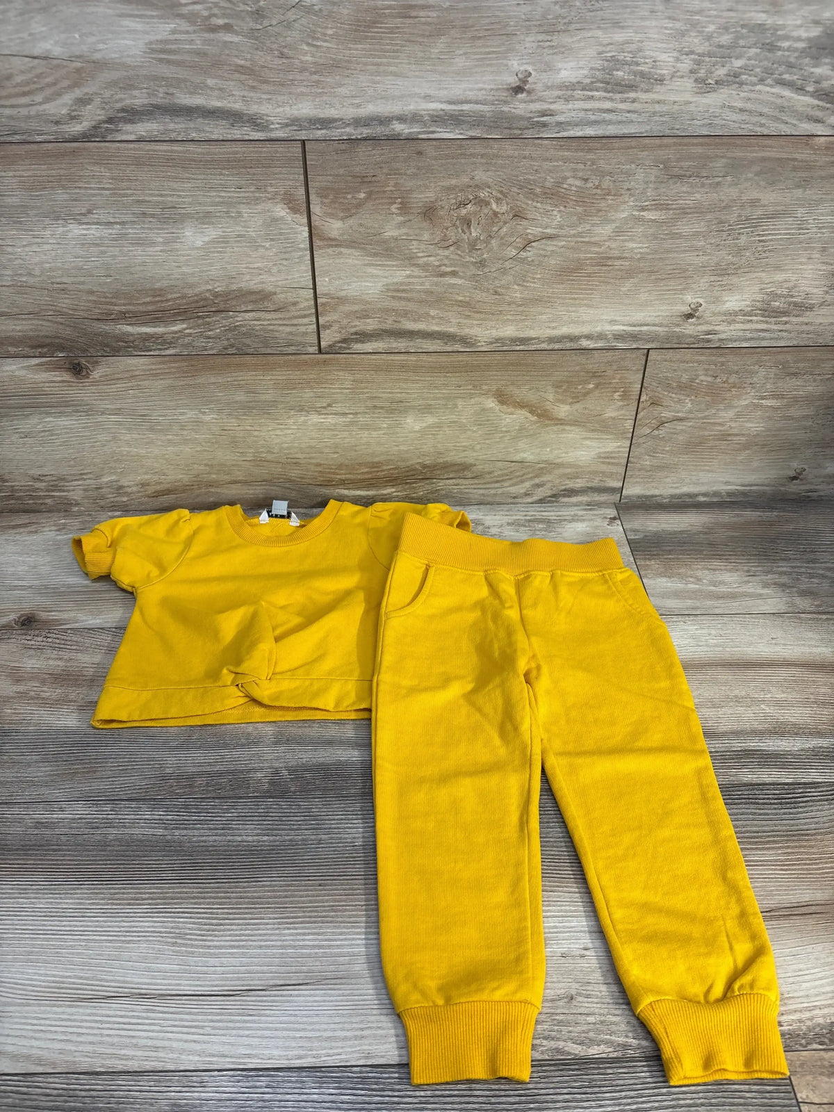 Bright yellow toddler outfit: short-sleeve top with front knot and matching jogger pants on wood floor