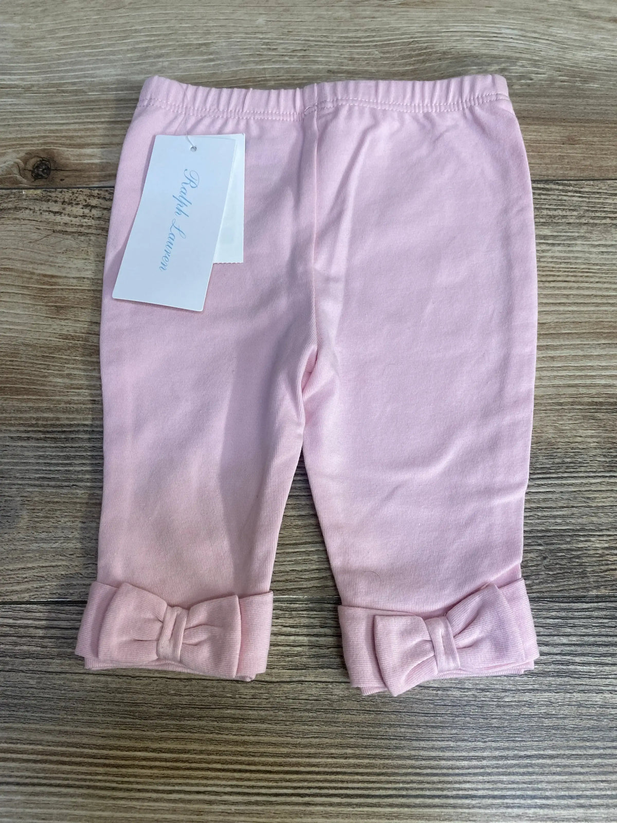 Flat lay of pink Ralph Lauren baby jersey leggings size 3 months showcasing elastic waistband and bow cuffs on wood background