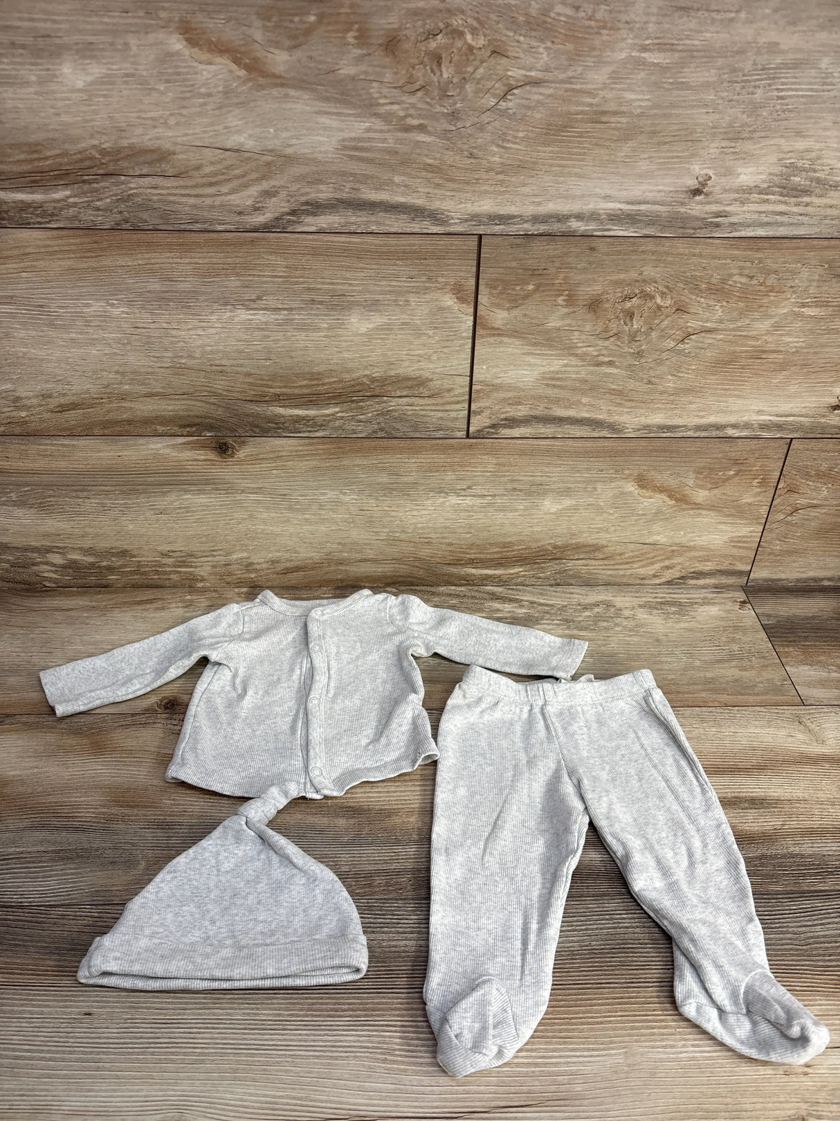 Light gray ribbed baby outfit with long-sleeve top, footed pants, and knot hat on wooden floor