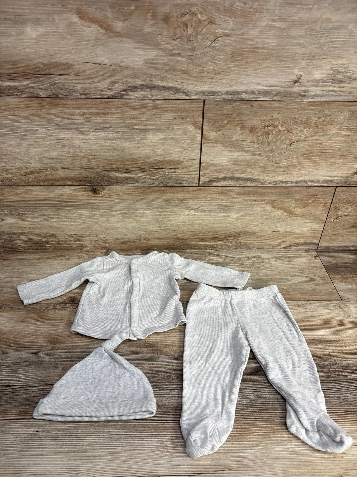 Light gray ribbed baby outfit with long-sleeve top, footed pants, and knot hat on wooden floor