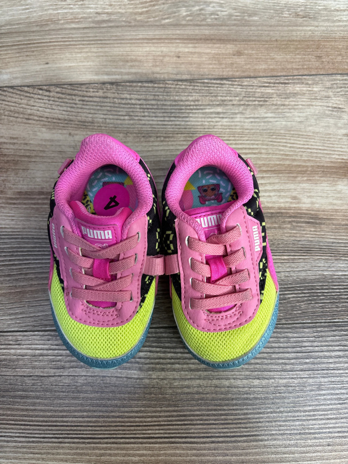 Pair of colorful Puma toddler sneakers with pink, yellow, and black design on wooden floor