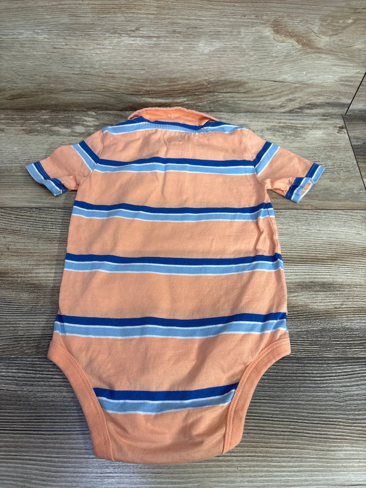 Peach baby onesie with blue and white horizontal stripes on wooden floor, children's clothing