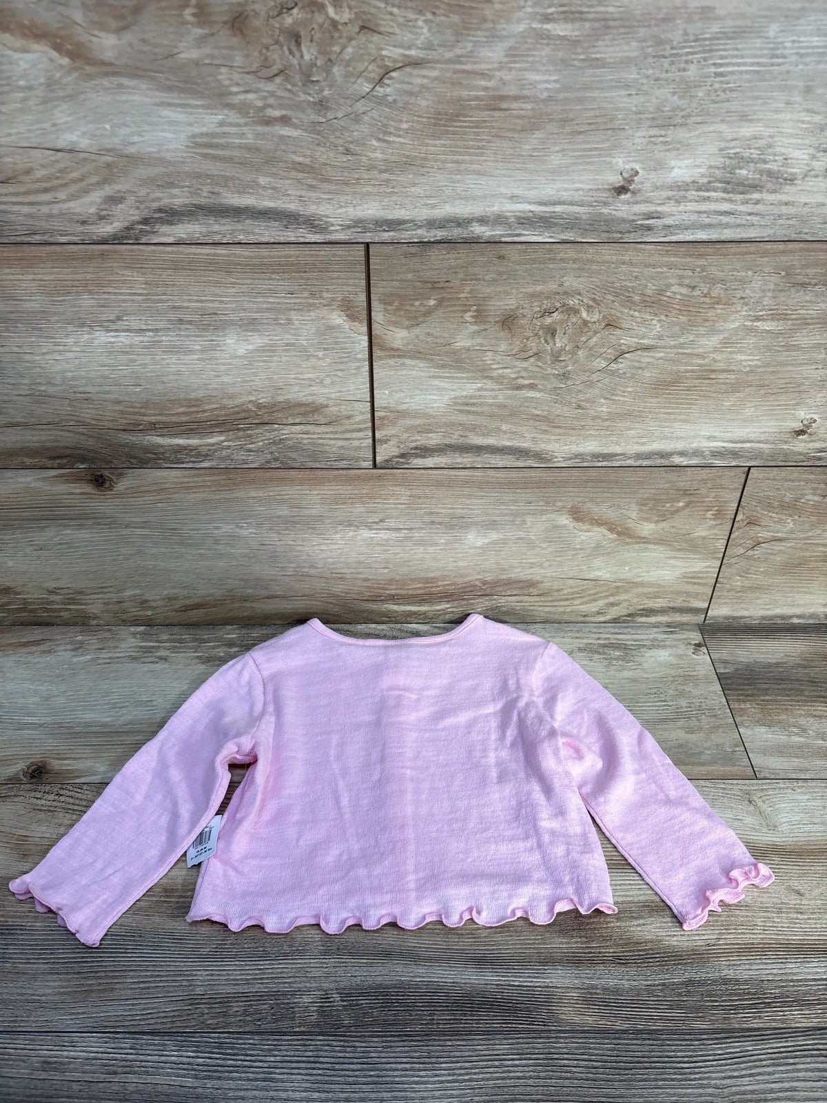 Back view of pink Old Navy button-up cardigan, showing long sleeves and ruffled hems on a wood-look background