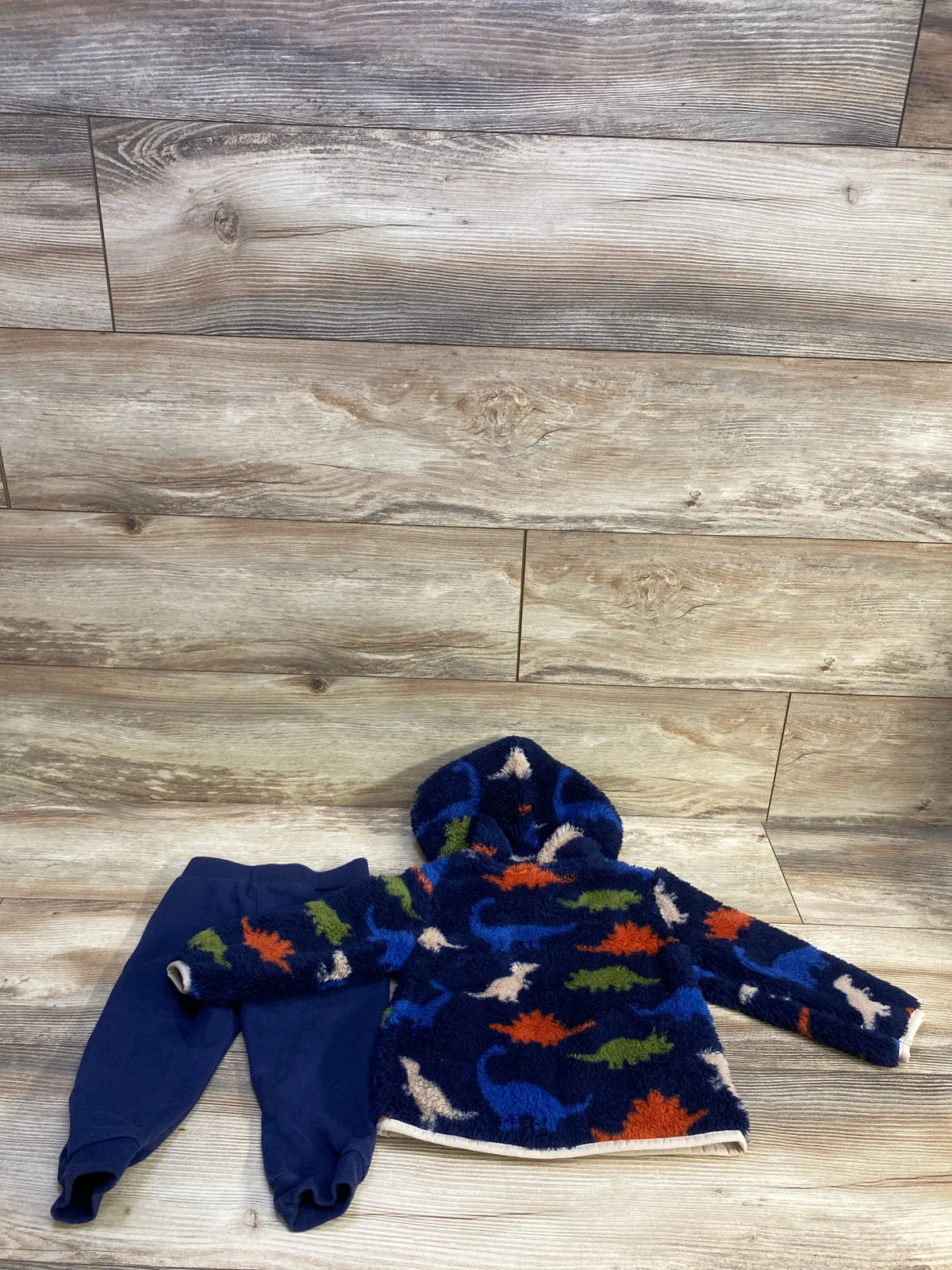 Front view of 2-piece navy faux-fur hooded jacket with multicolor dinosaur print and matching navy pants on wood backdrop