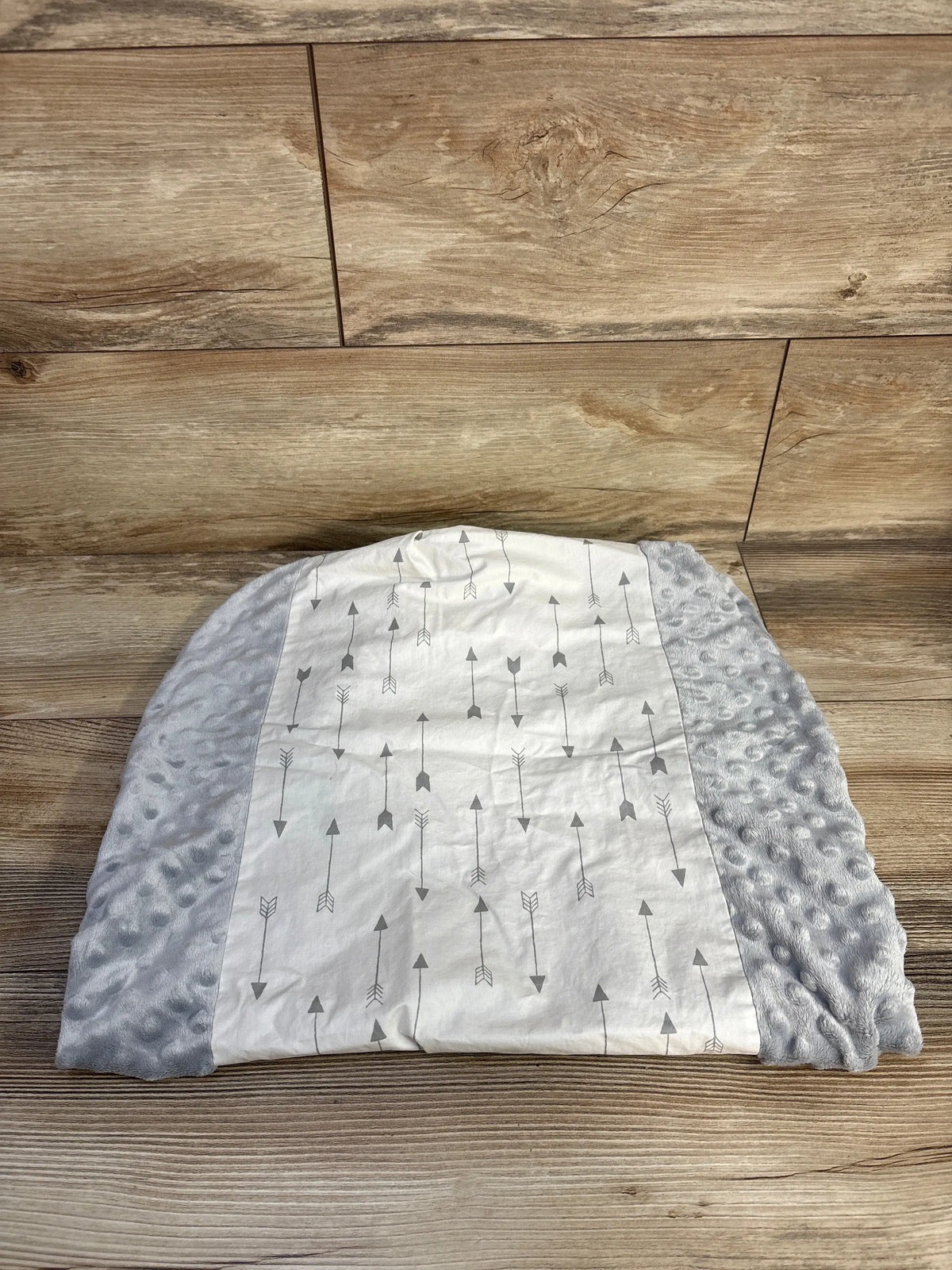 Top view of Cloud Island Arrow Changing Pad Cover showcasing gray plush sides and a white arrow pattern on a wood floor