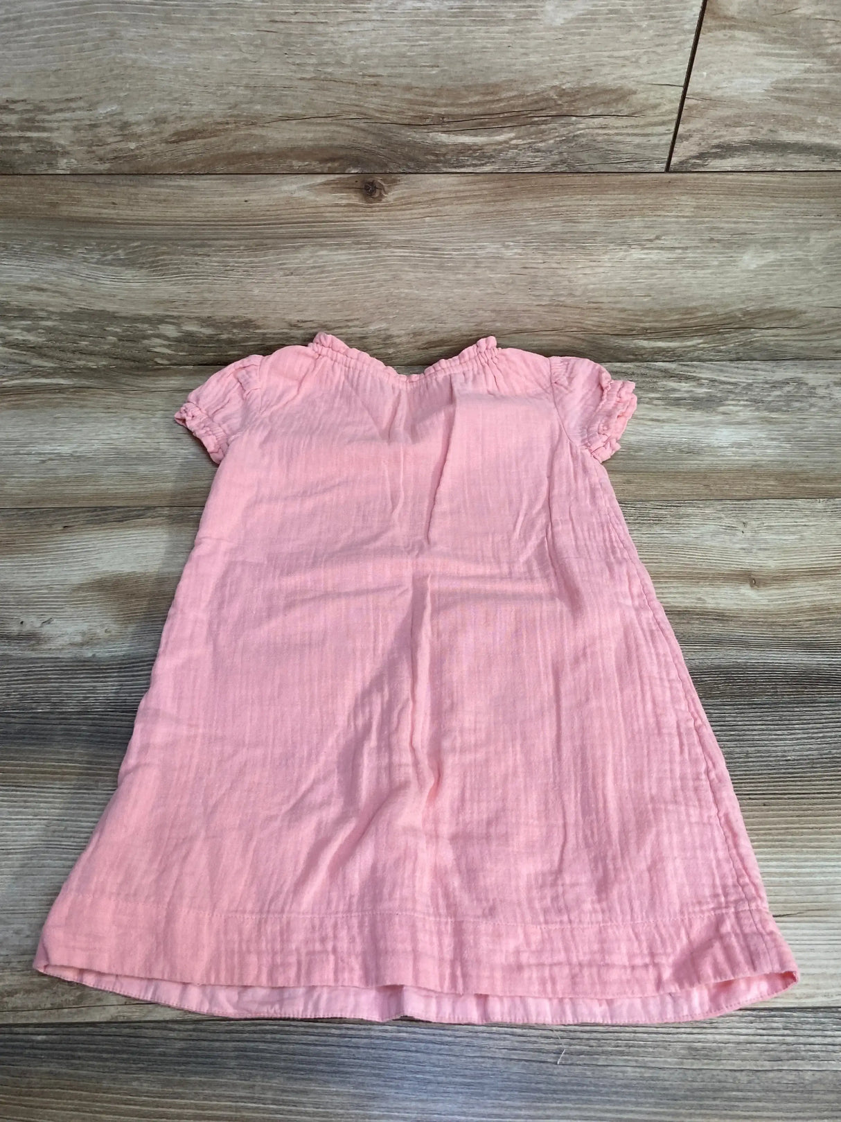 Flat lay front of Baby Gap pink embroidered dress showcasing short ruffle sleeves and gathered elastic neckline on wood background
