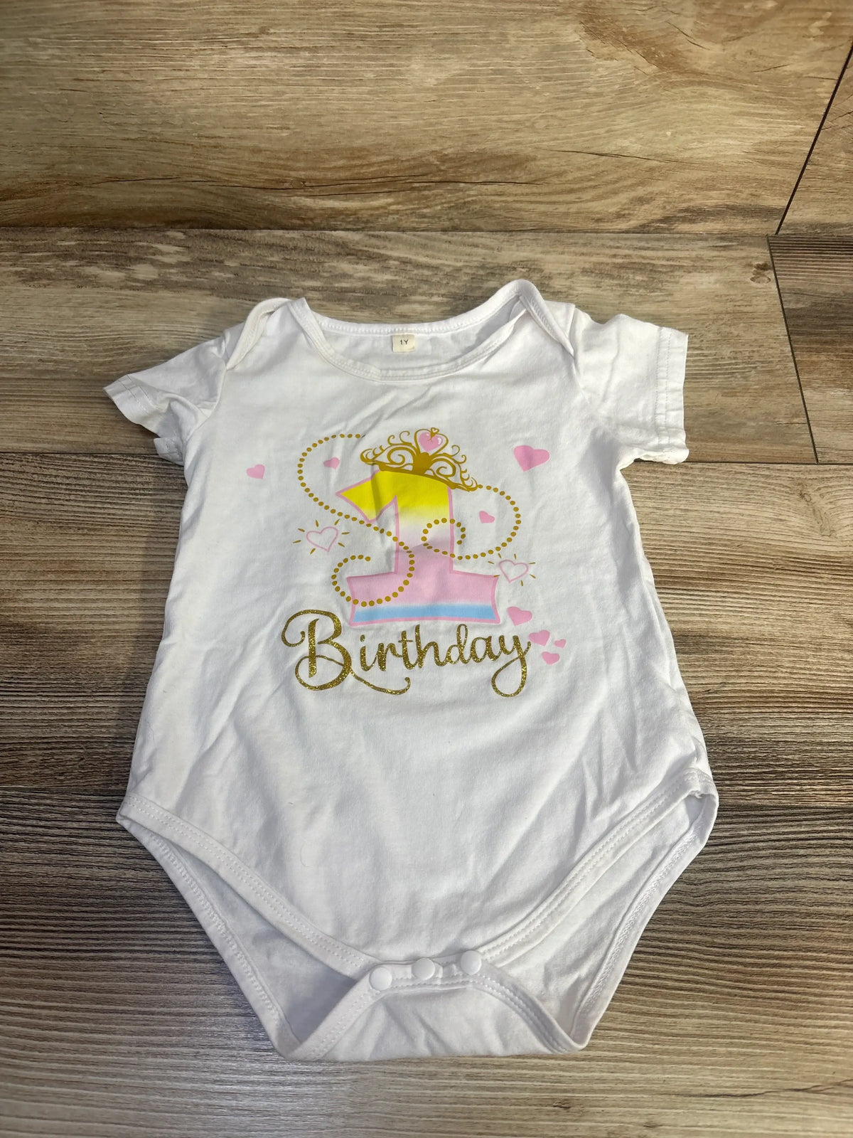 Front view of white first birthday bodysuit with princess graphic, hearts, and gold Birthday lettering on wood background