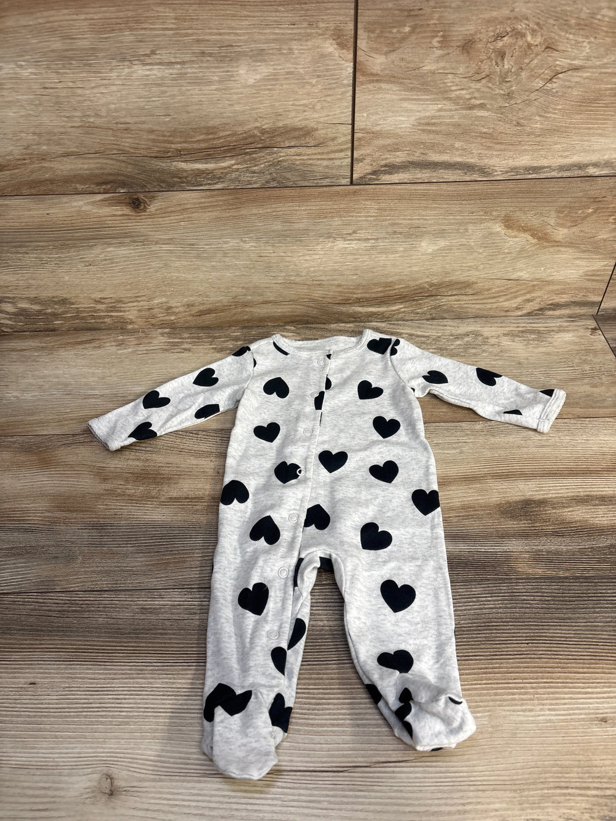 Gray baby onesie with black heart print, long sleeves, and snap buttons, on wooden floor