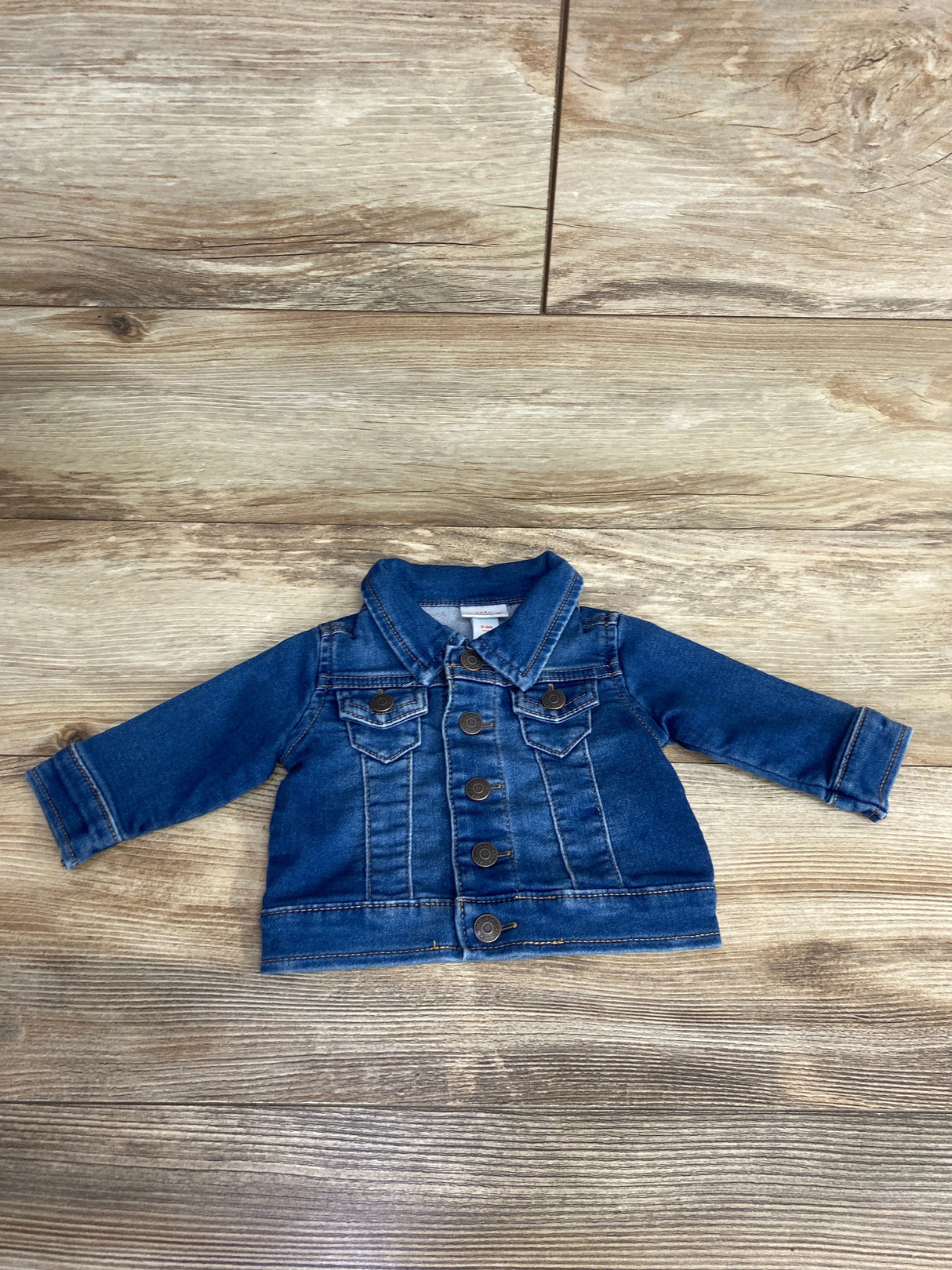 Toddler blue denim jacket with button-up front and chest pockets on wooden floor