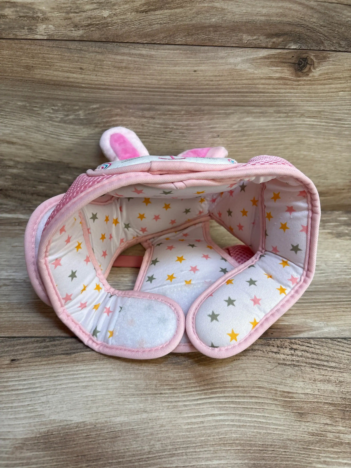 Pink padded baby safety helmet with star print and bunny ears on wooden background