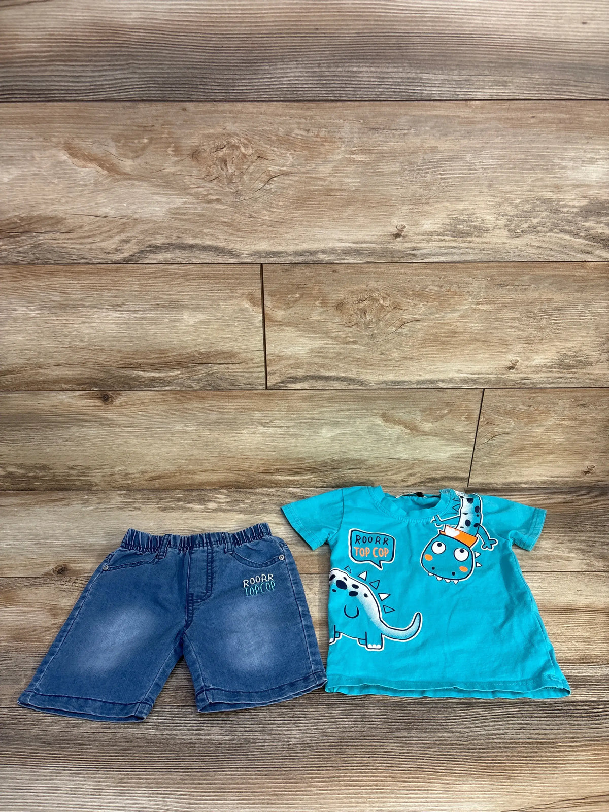 Flat lay of blue Pansee two-piece shirt and shorts set with dinosaur graphics and elastic waistband