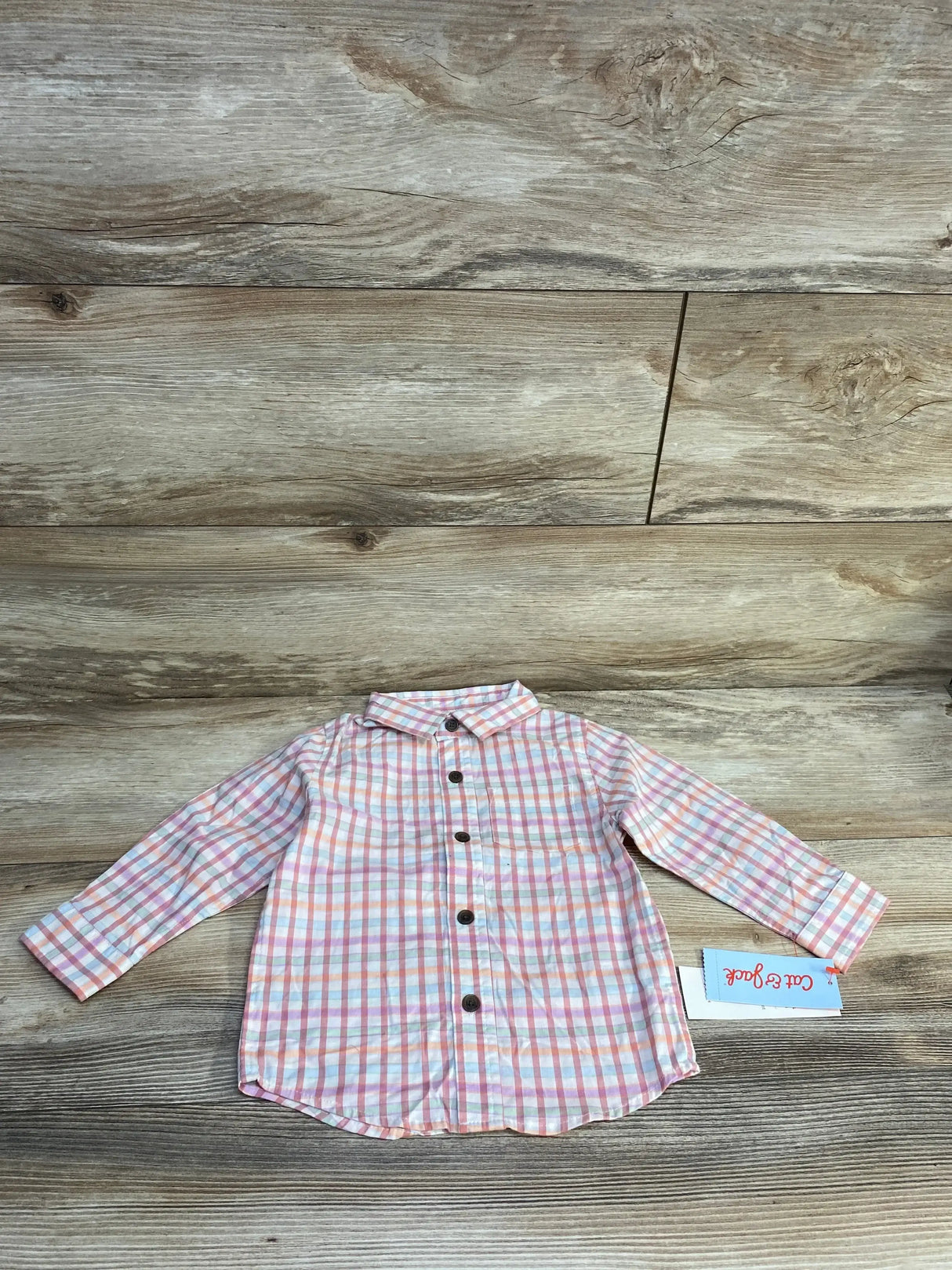 Flat lay of Cat and Jack pink and orange plaid button-up toddler shirt size 18 months, long sleeves and brown buttons, wood background
