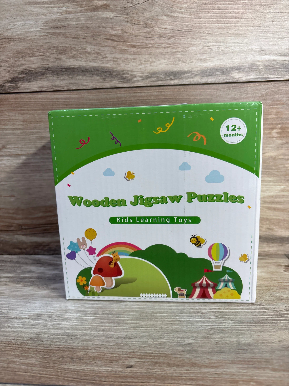 Front view of wooden jigsaw puzzles box showcasing colorful animal illustrations and "12+ months" age label on wooden tabletop