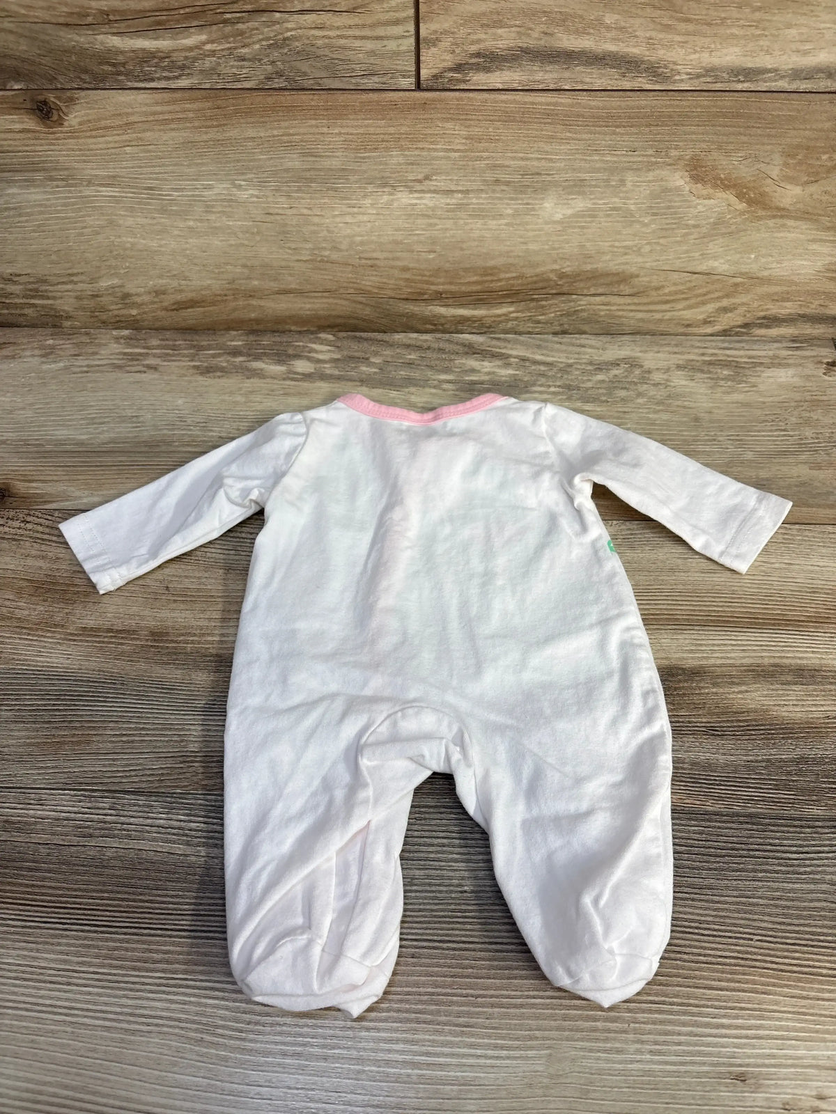 Back view of white footed newborn ballerina sleeper size 0-1M showcasing pink neckline trim and long sleeves on wood floor
