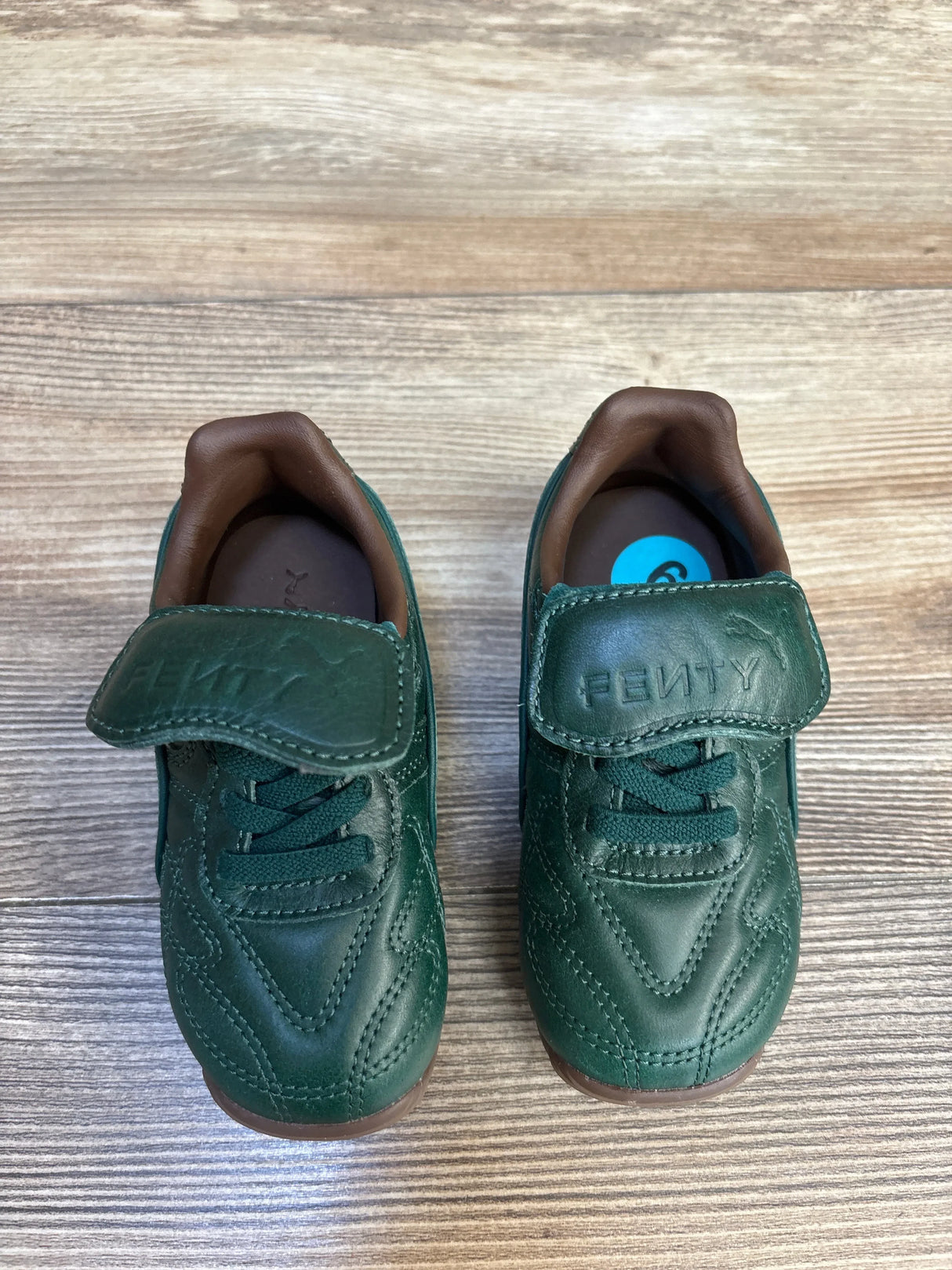 Green Fenty toddler sneakers with velcro straps on wooden floor
