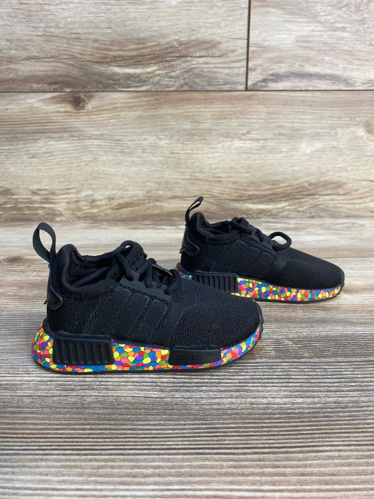 Black kids athletic sneakers with colorful mosaic soles on wood floor background