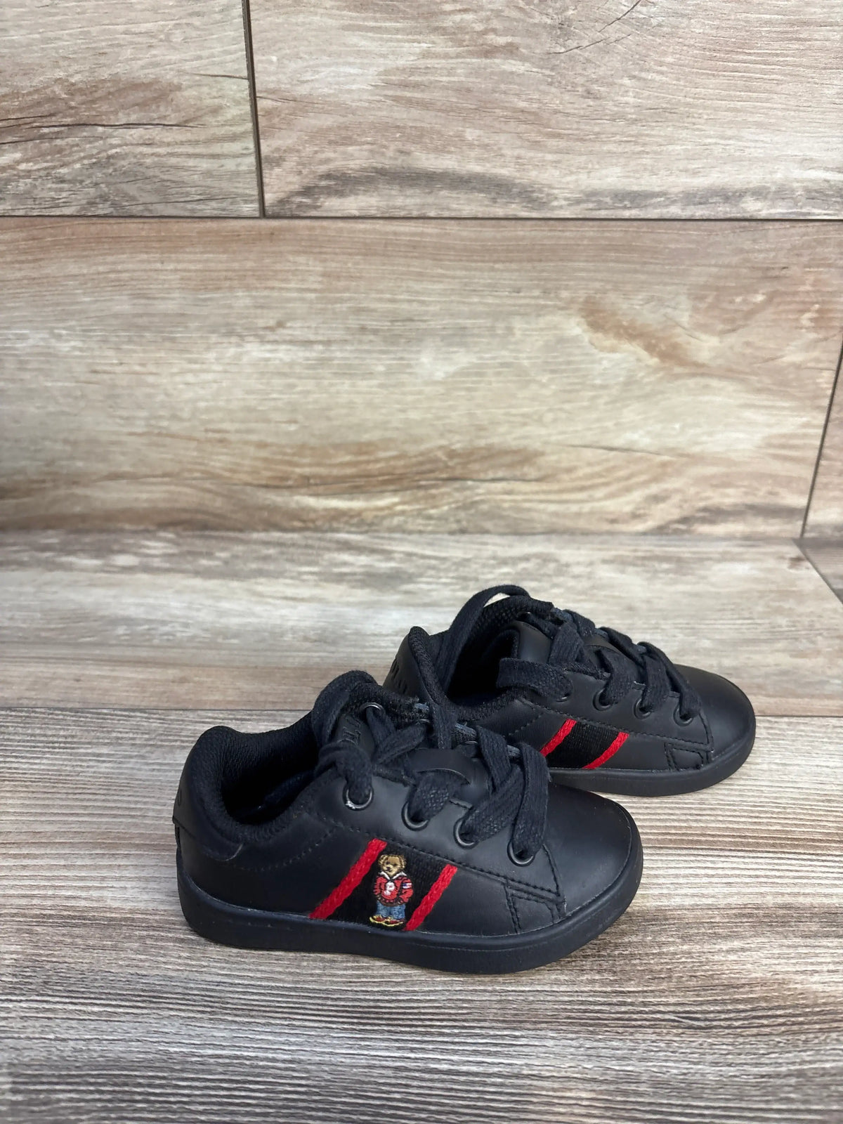 Angled view of black Polo Ralph Lauren Quilton Bear sneakers in size 6C showcasing an embroidered Polo Bear and red stripes on a wood floor