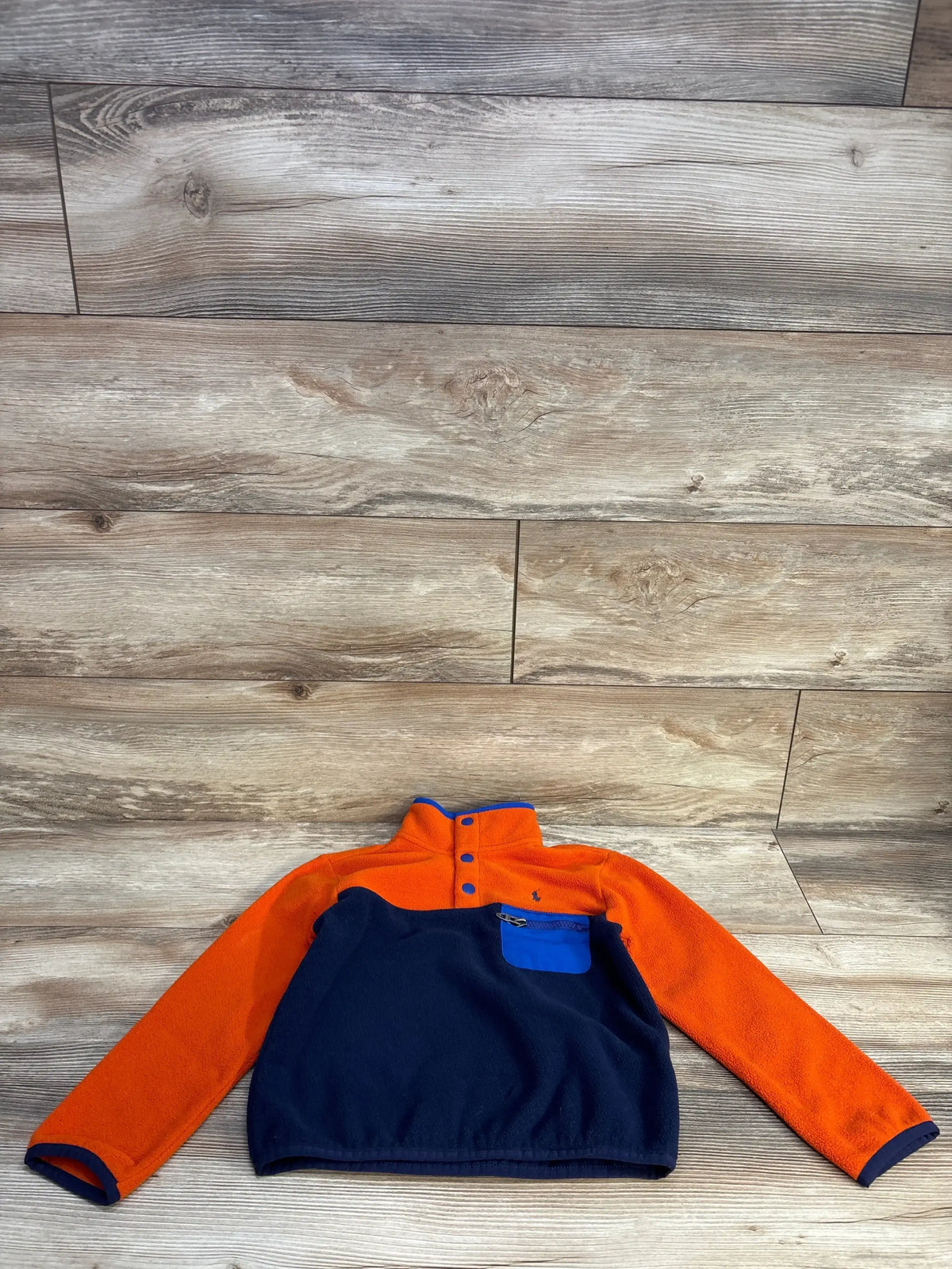 Orange and navy blue fleece pullover with blue zippered chest pocket on wooden floor