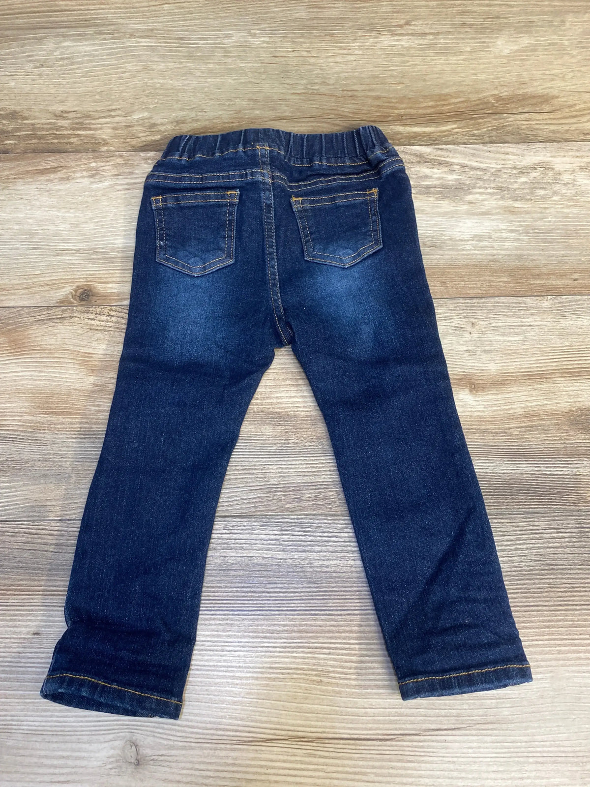 Toddler dark wash denim jeans with elastic waistband, back pockets, on wood surface