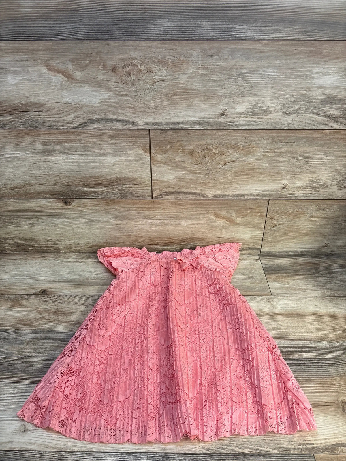 Pink lace baby dress with ruffled sleeves and pleated skirt on wood floor