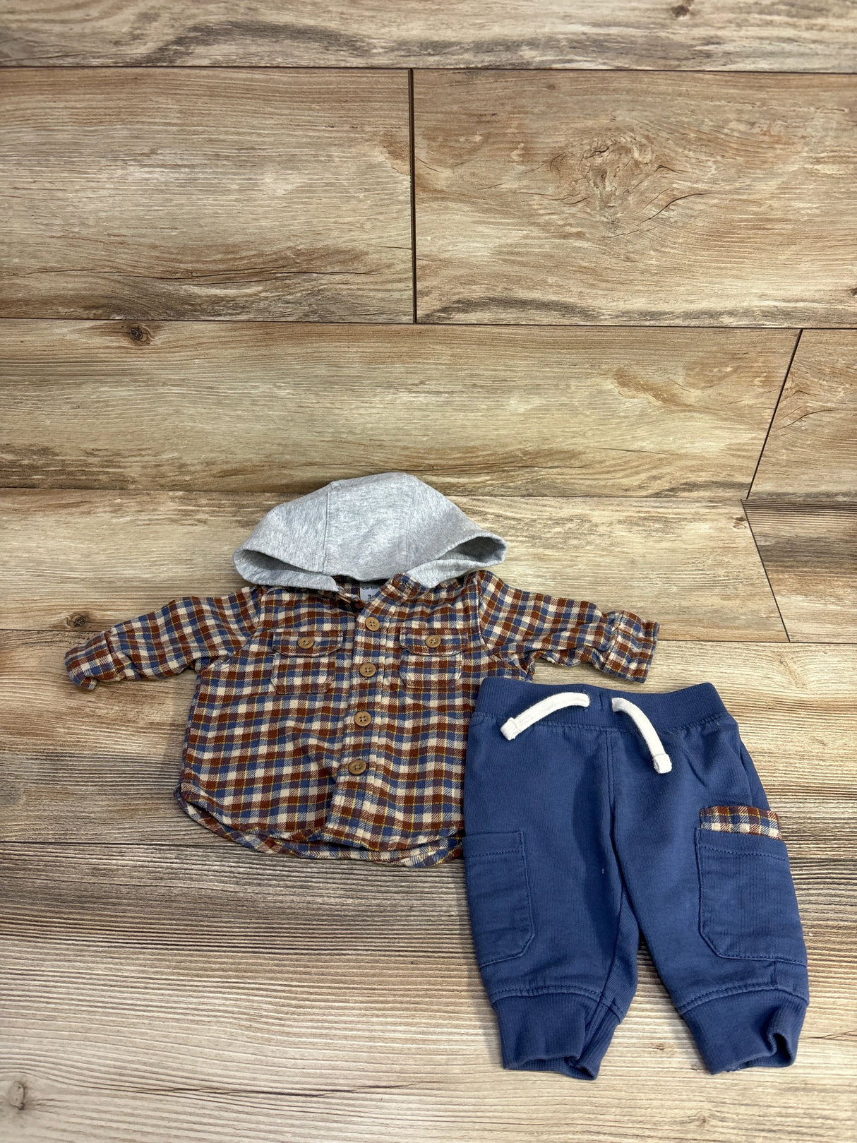 Baby outfit with blue and brown plaid hooded flannel shirt and blue pants with drawstring and pockets on wood floor