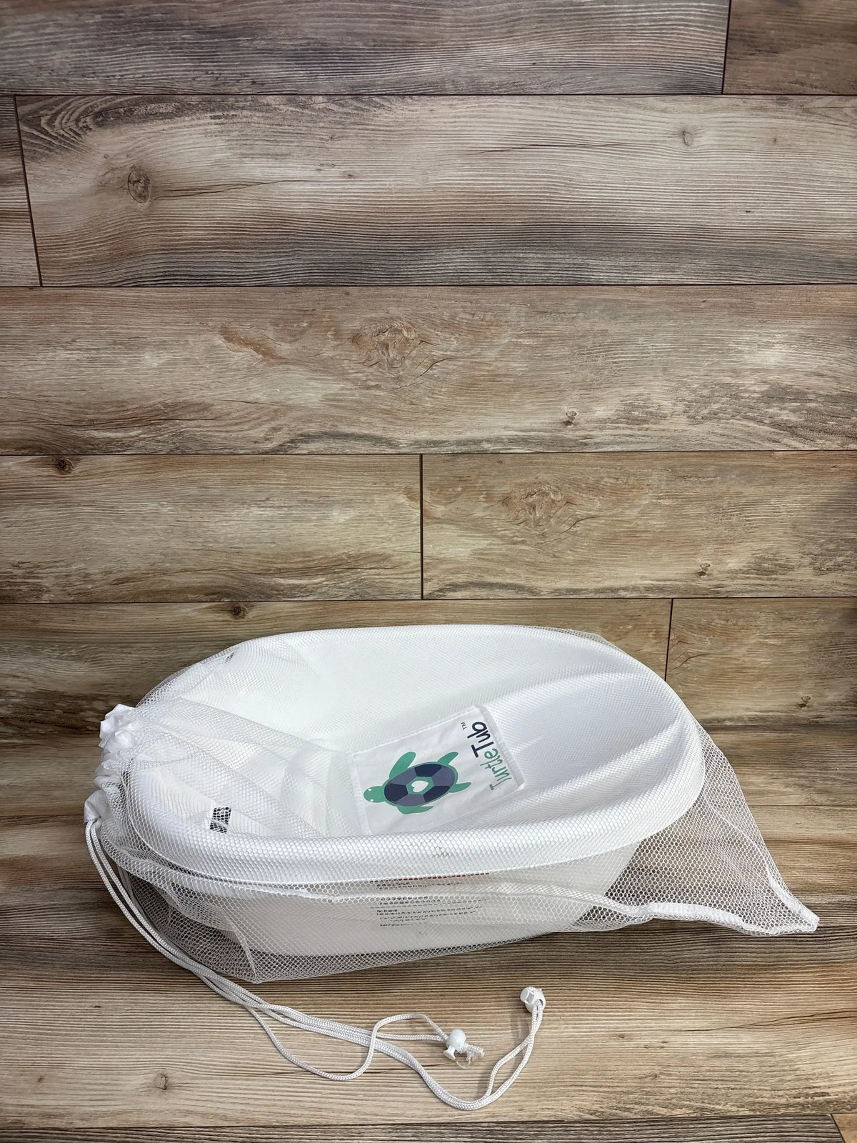 White baby bath support with mesh cover and drawstring on wood floor