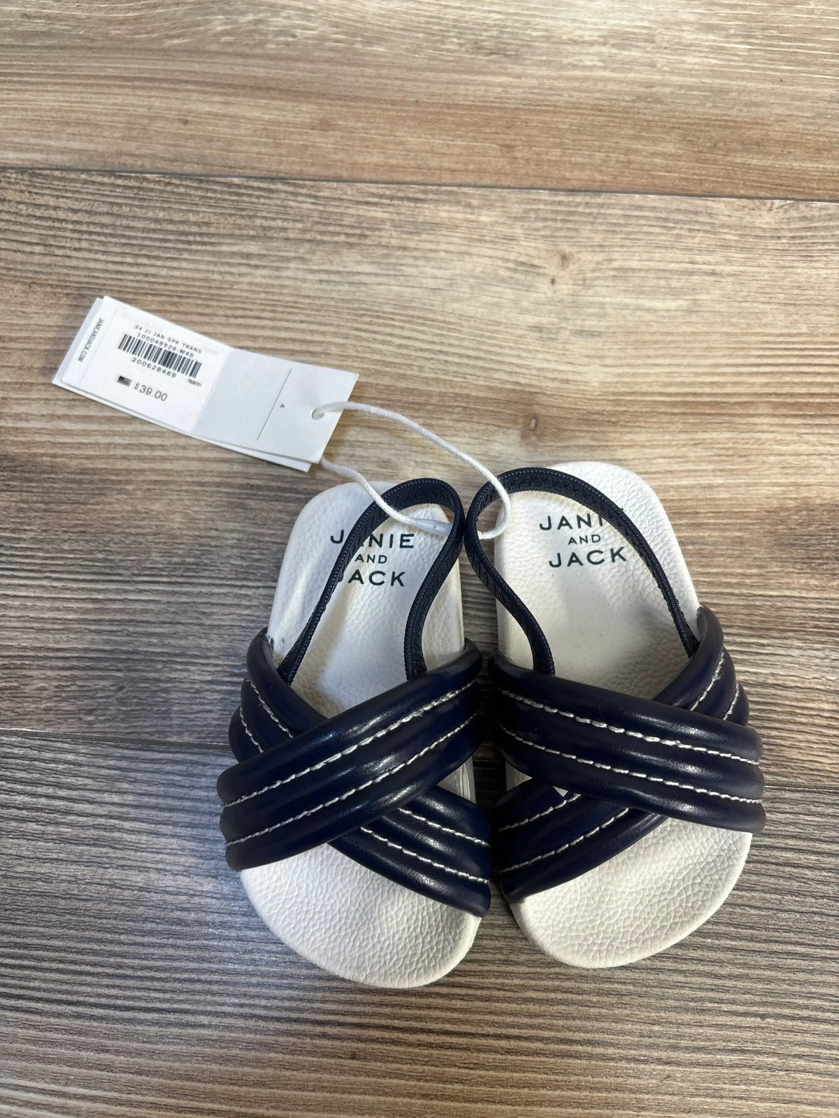 Navy and white Janie and Jack baby sandals with tag on wood background.