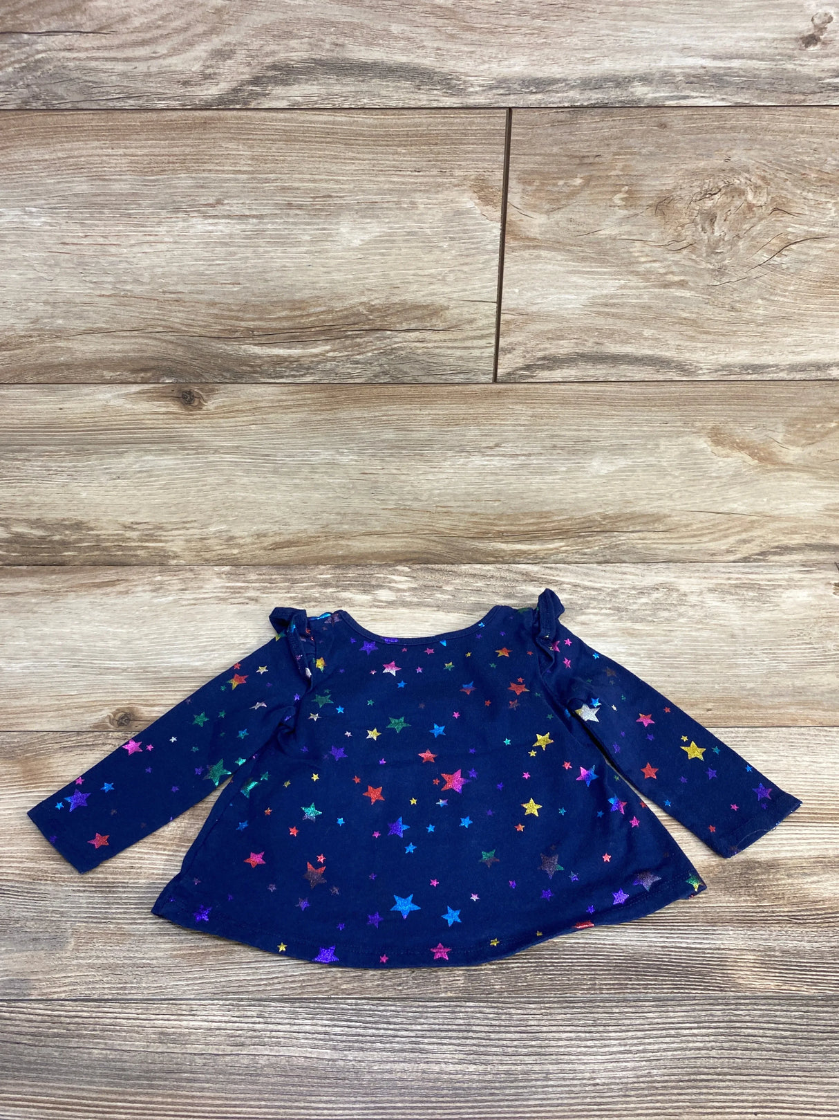 Navy blue long-sleeve baby shirt with colorful star pattern on wooden floor