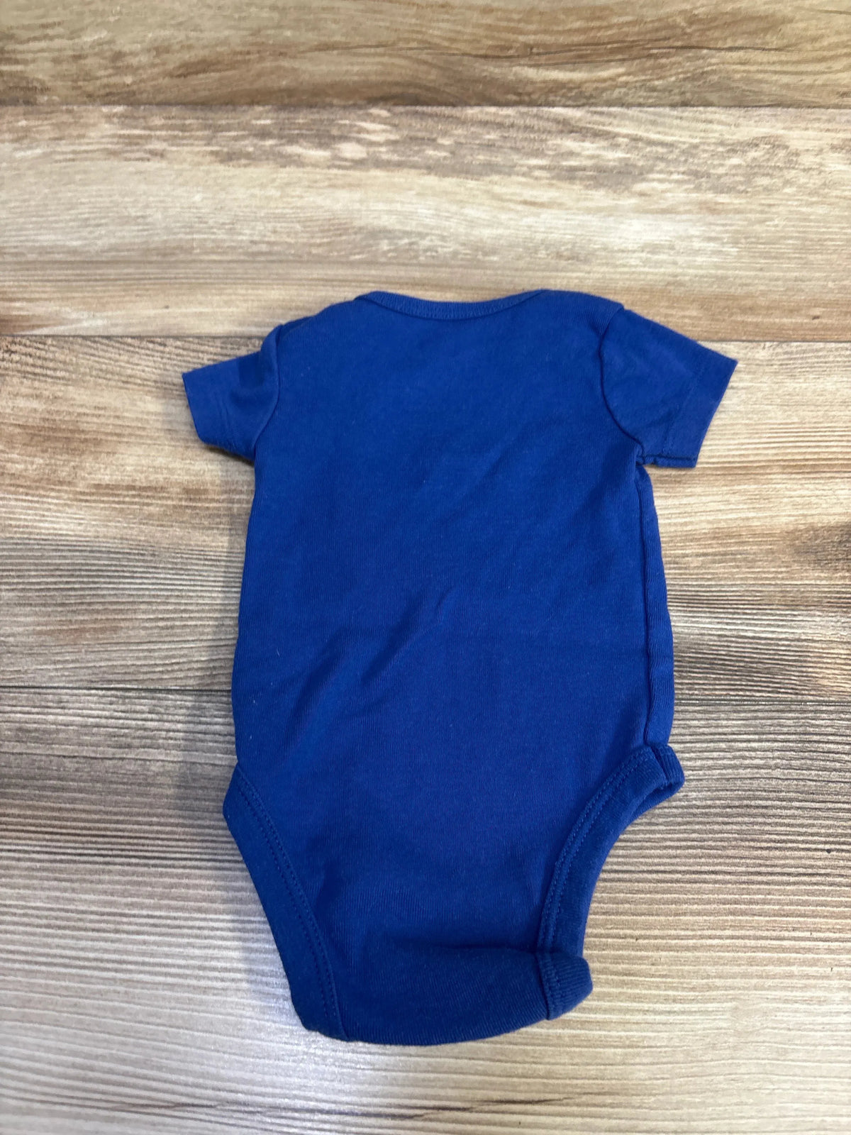 Back view of Nike blue short-sleeve baby bodysuit (6M) showing snap leg openings on wood background