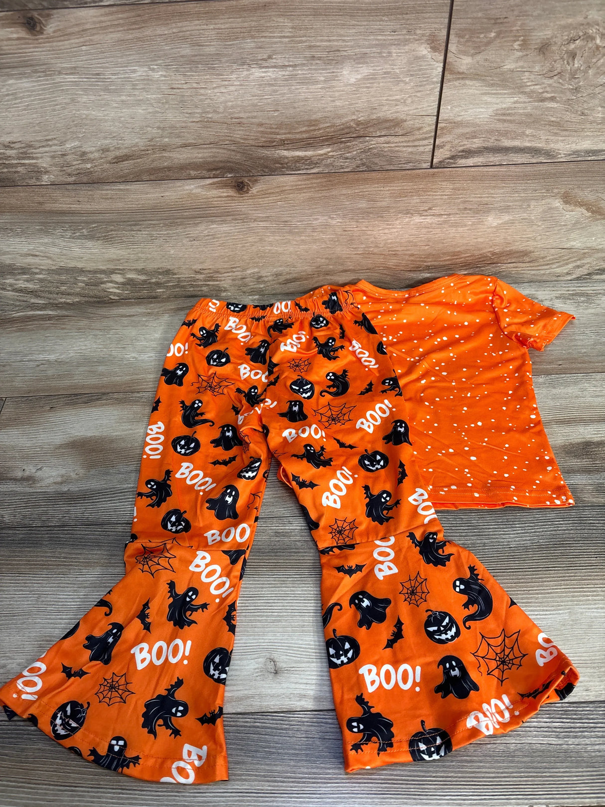 Orange Halloween kids pajamas with ghosts, pumpkins, BOO! print, and polka dot top on wood floor