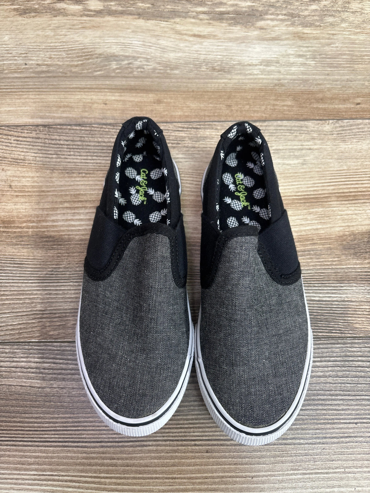 Top view of Cat & Jack gray canvas slip-on sneakers, size 13C, with pineapple-print lining and white soles on wood grain